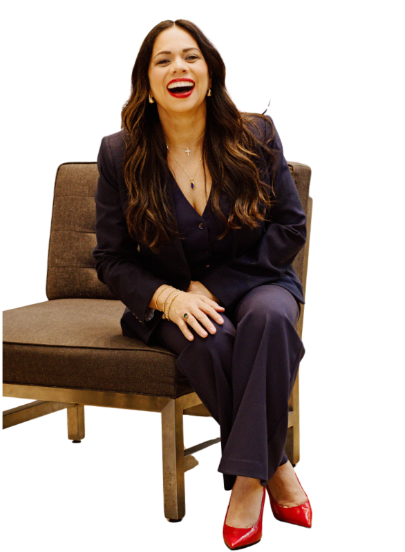 Esme Graff  sitting on a brown chair, smiling, wearing a navy blazer and pants, red high heels, and jewelry.