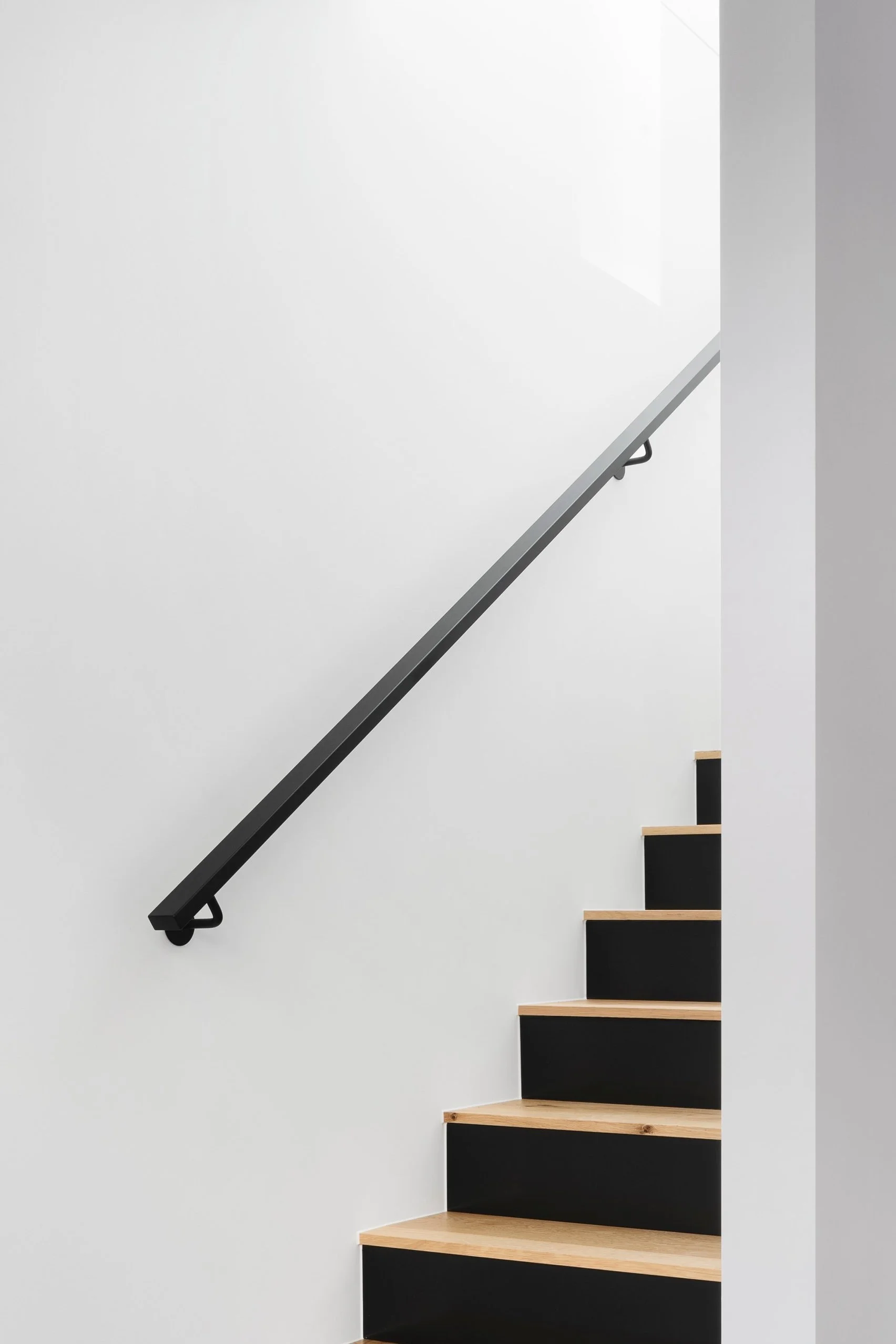 Minimalist interior with a black staircase and handrail against a white wall.