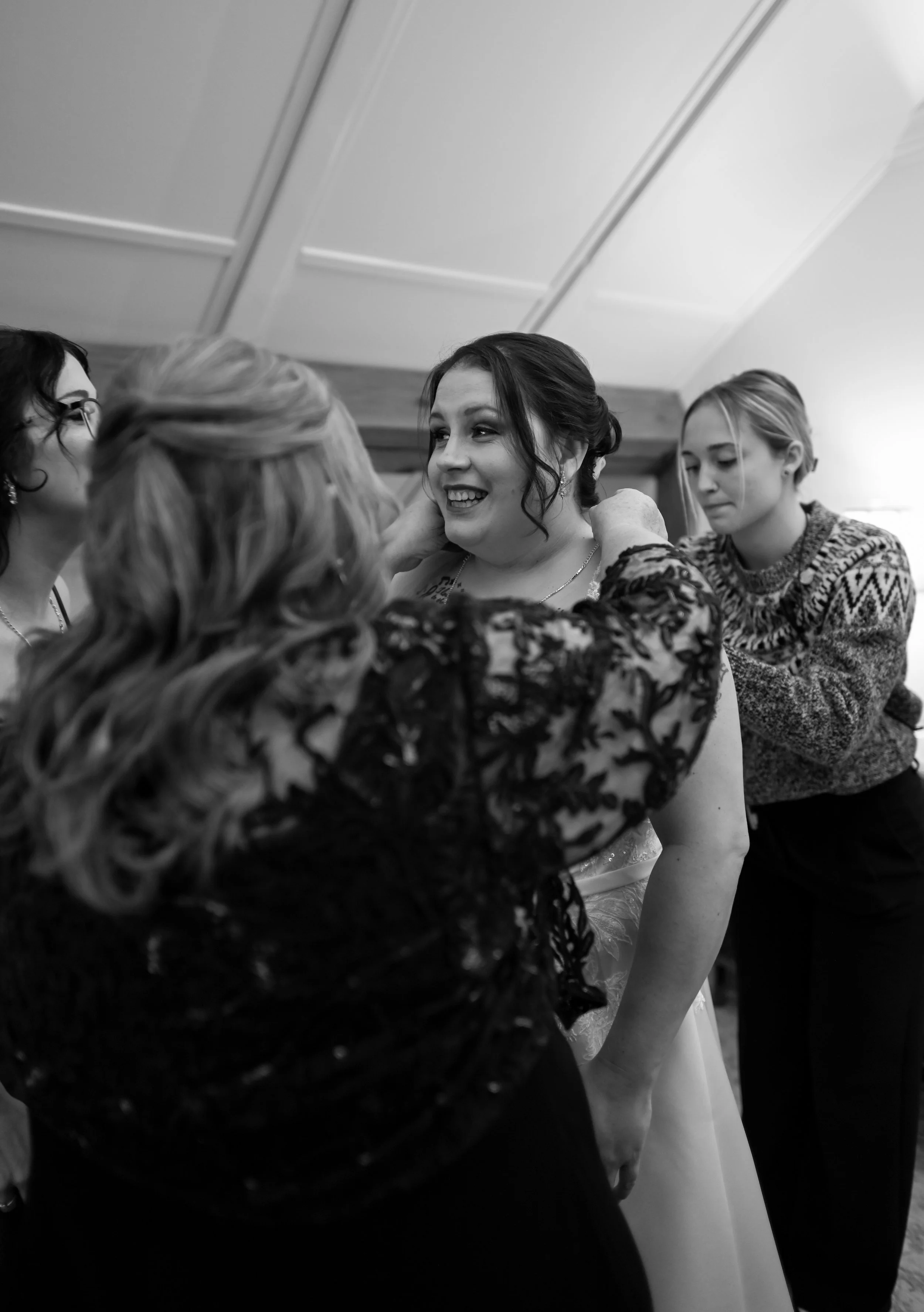 A bride getting ready with help from her friends or family, as the women adjust her dress and accessories in a cozy indoor setting.
