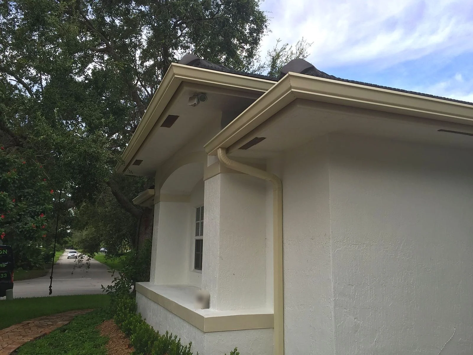 Cream seamless gutter and downspout on the corner of a Miami home under oak canopy