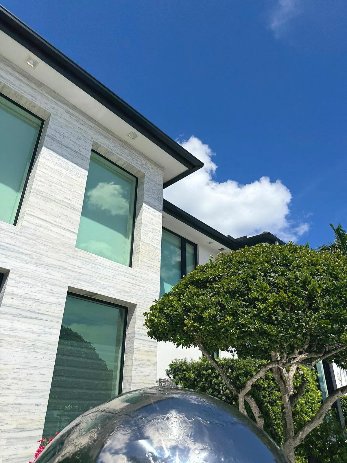 Black seamless gutter along the flat roofline of a modern stone-clad home in Miami