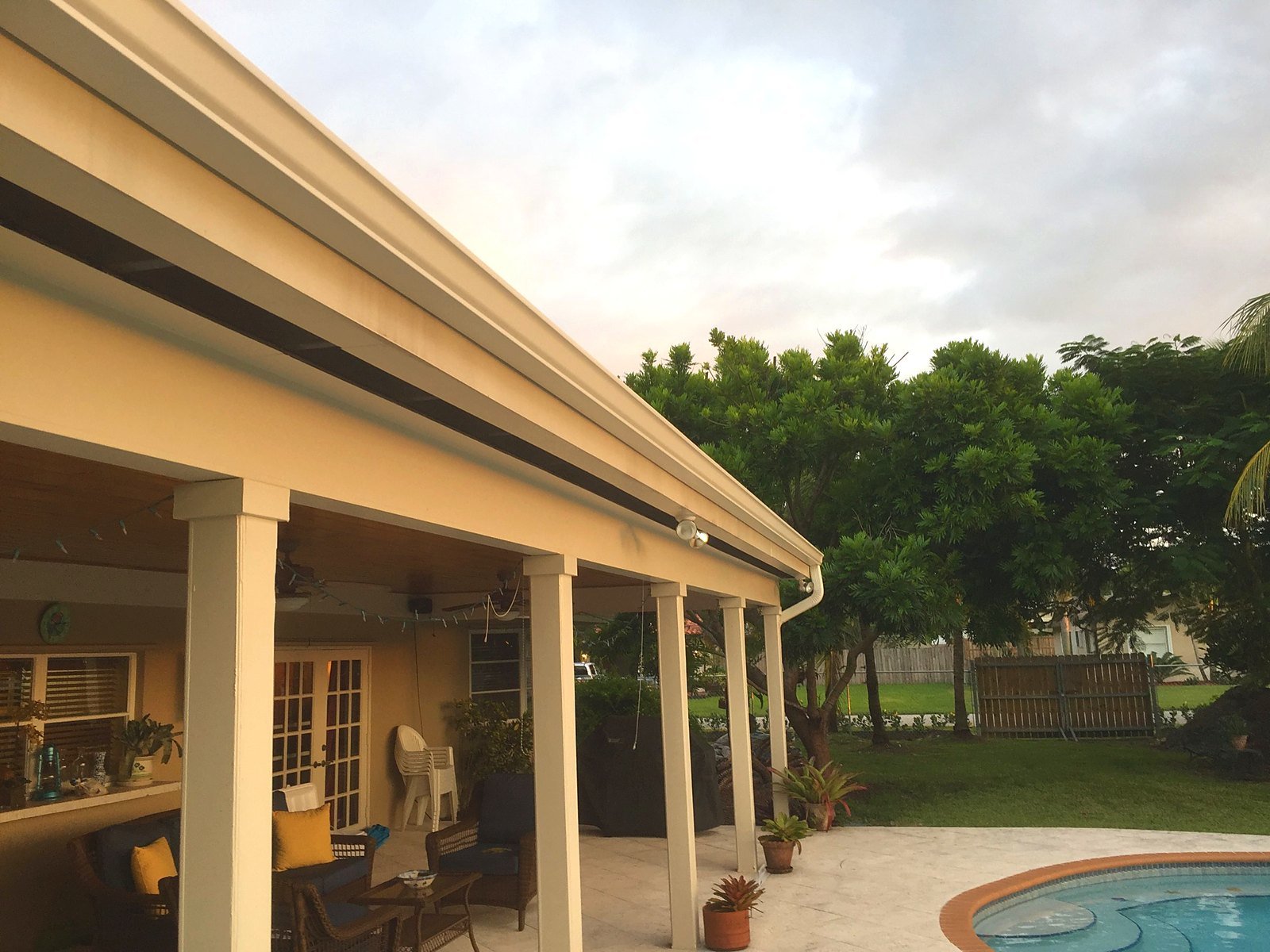 Cream seamless gutter running the length of a covered patio with a downspout at the corner on a Miami home