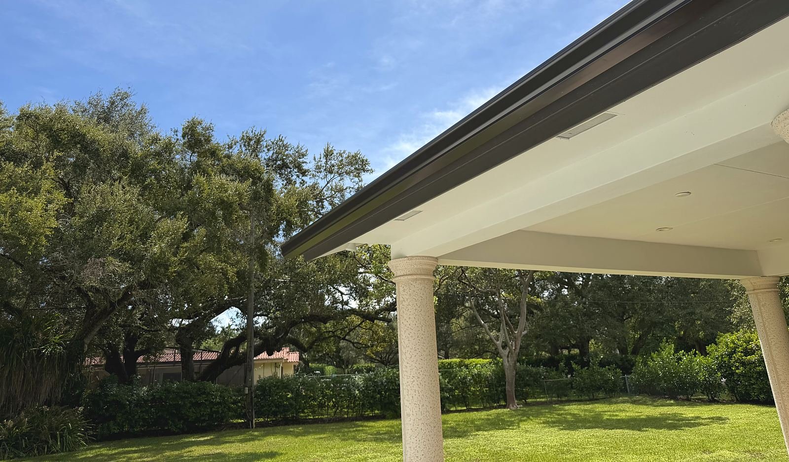 Long bronze seamless gutter run along a flat roofline on a Pinecrest home under live oak canopy