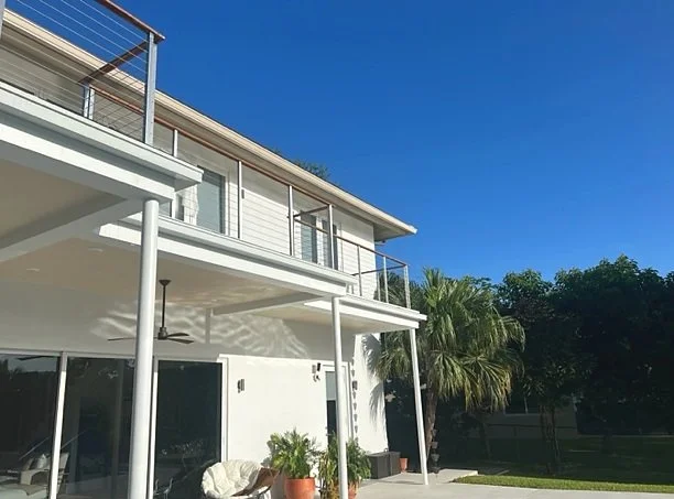 Contemporary Pinecrest home with white seamless gutters along a flat roofline and rain chains in place of downspouts