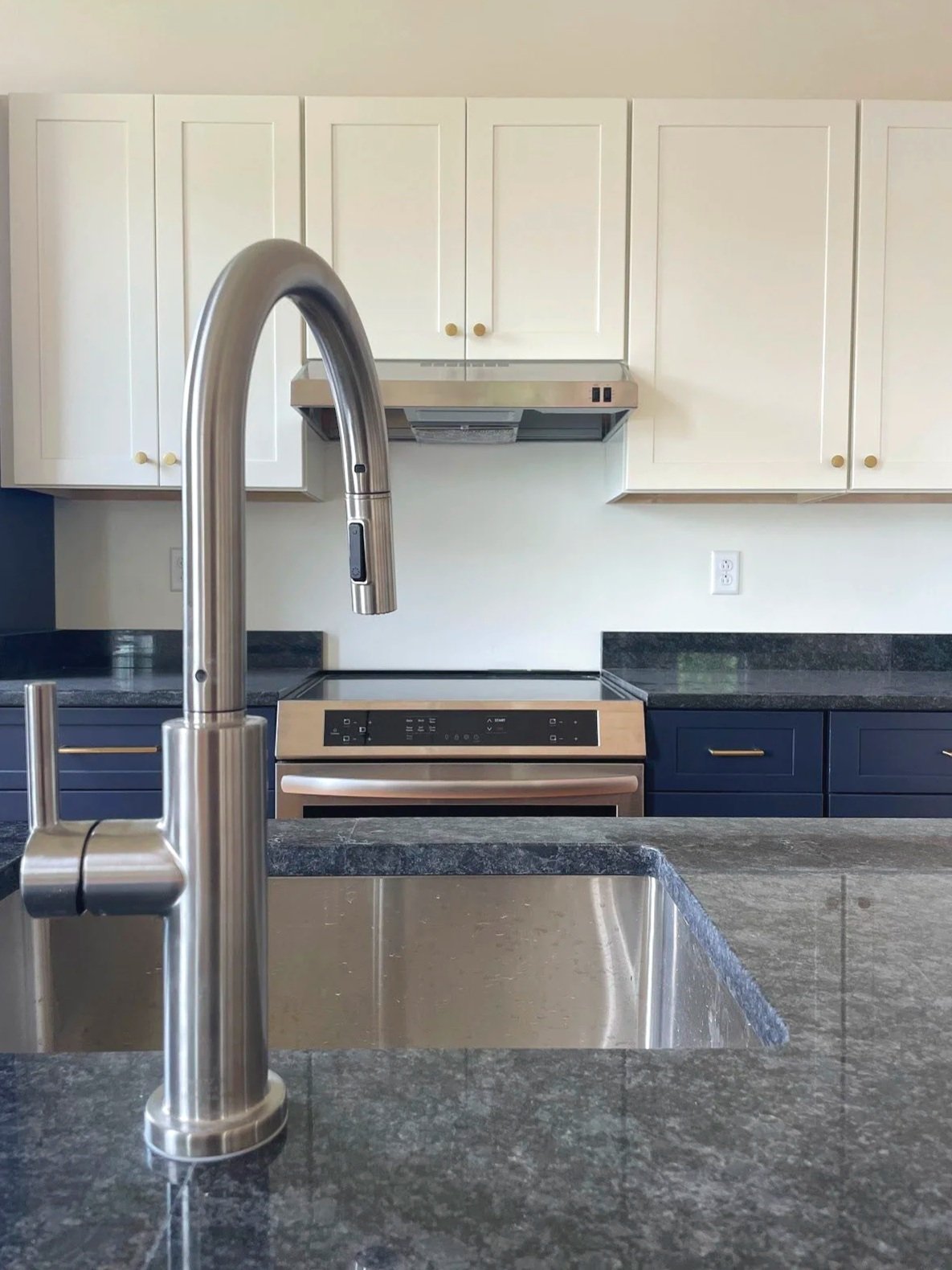 Modern kitchen with stainless steel sink, black granite countertops, white upper cabinets, navy blue lower cabinets, and a stainless steel stove and range hood.