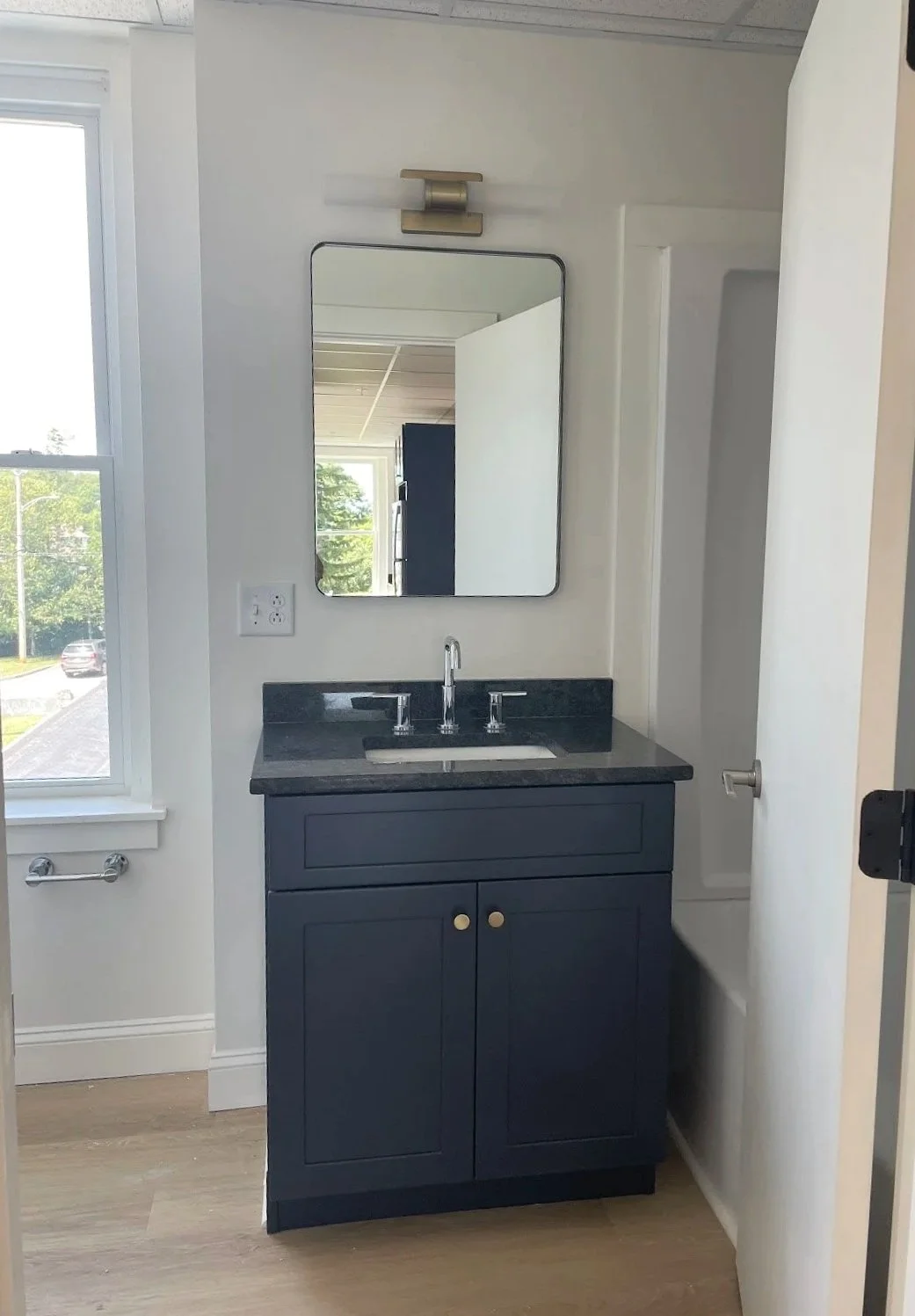 Small bathroom with a dark blue vanity, white walls, a mirror, a window, and a black countertop.