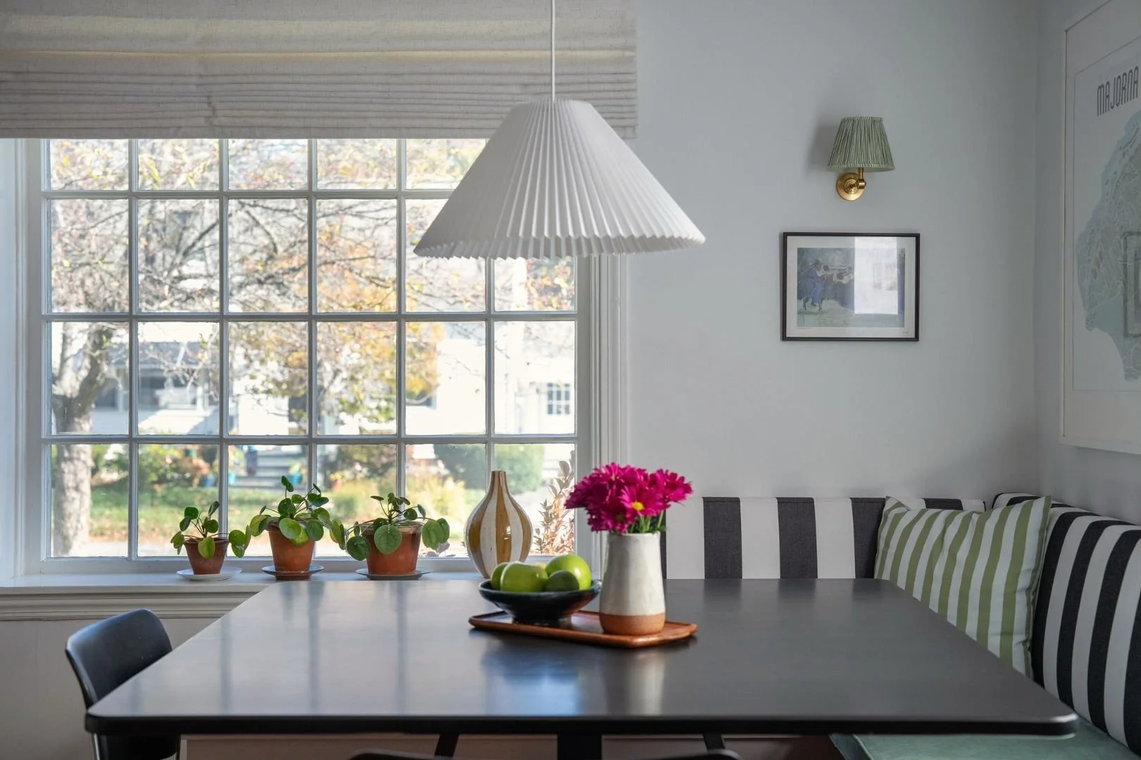Breakfast nook with built in bench and tailored striped cushions, black dining table and Scandinavian pendant light and art. Rechargeable wall-mounted sconce without cord. 
