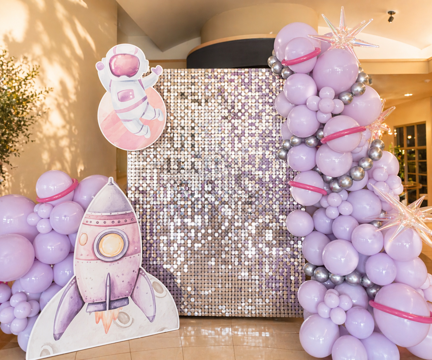 Decorative outdoor setup for Autumn's Dollhouse, featuring a pink, purple, green, and white balloon arrangement, holographic backdrop with purple text, and cartoon cutouts of a smiling girl with curly hair hugging a white cat with a pink bow and a mermaid character with big eyes and colorful scales.