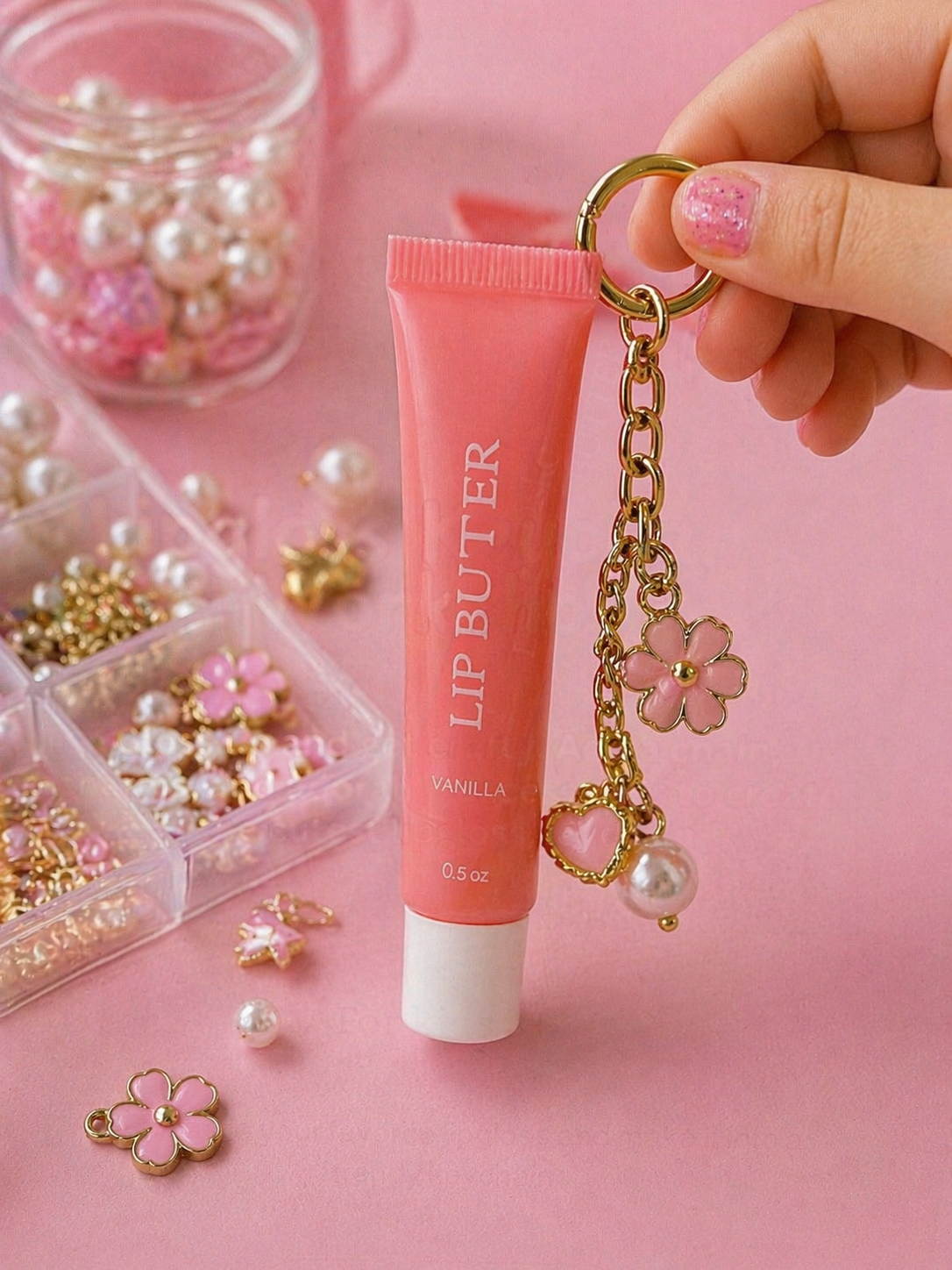 Pink lip gloss tube with gold chain and charm accessories, opened lip gloss container, decorative box with ribbon, and text overlay promoting a lipgloss keychain workshop.