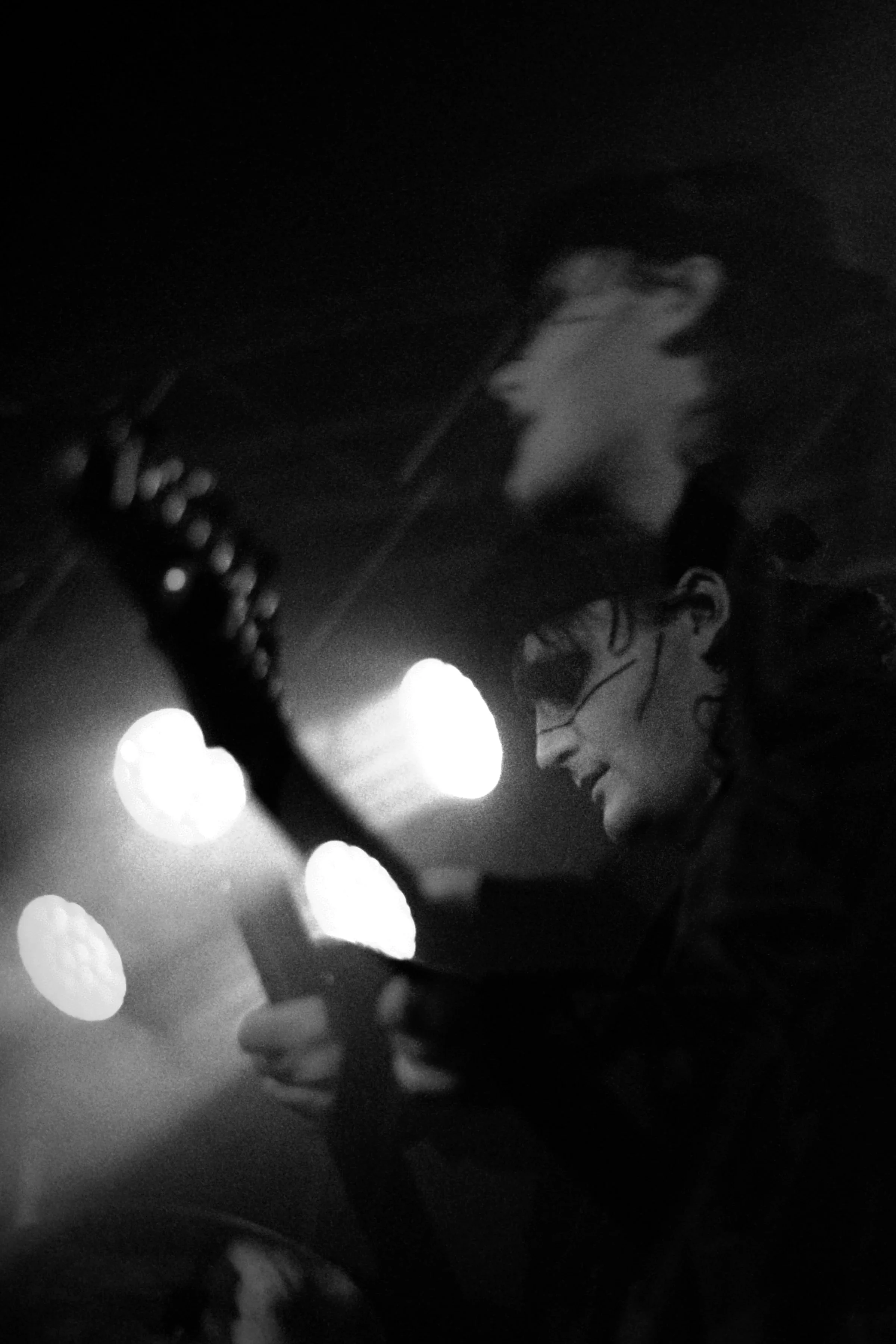 A person playing an electric guitar at night, with bright circular lights illuminating the scene and their face illuminated by the guitar's strings.