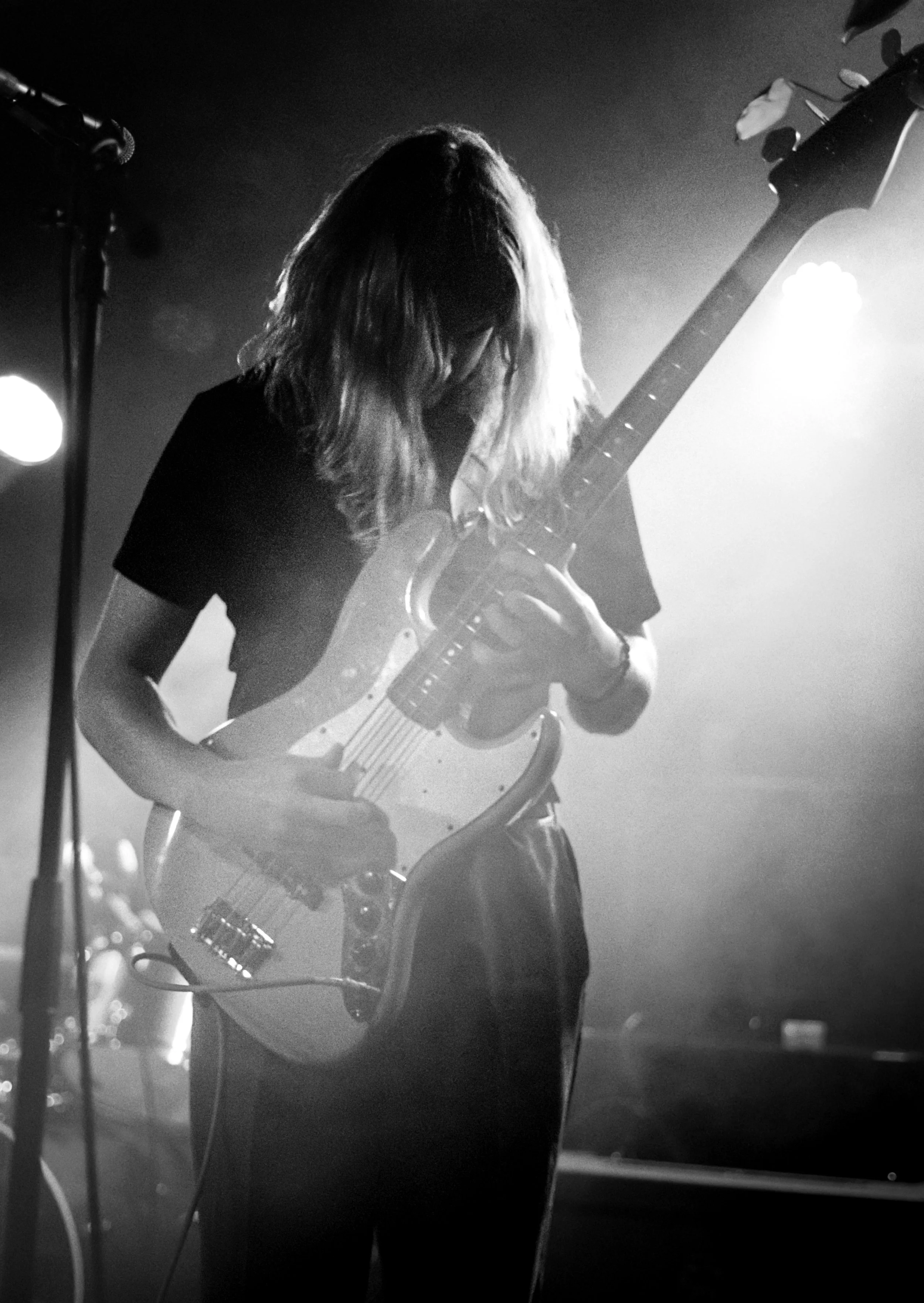 A woman with long hair playing an electric guitar on stage in black and white.