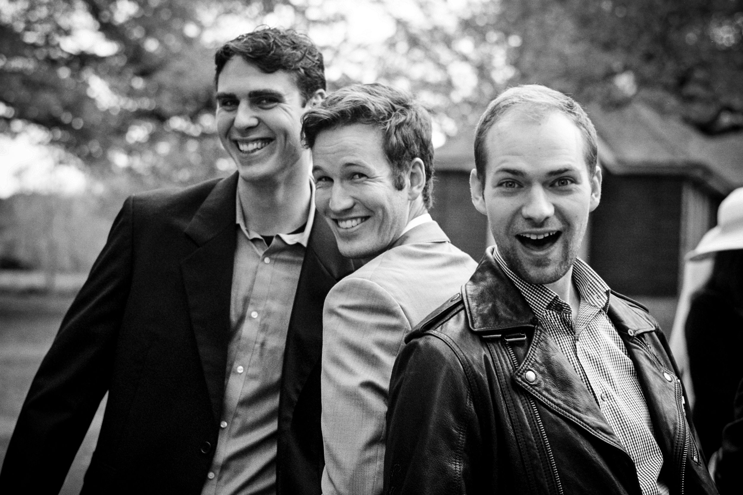 Black and white photo of three smiling young men standing outdoors.