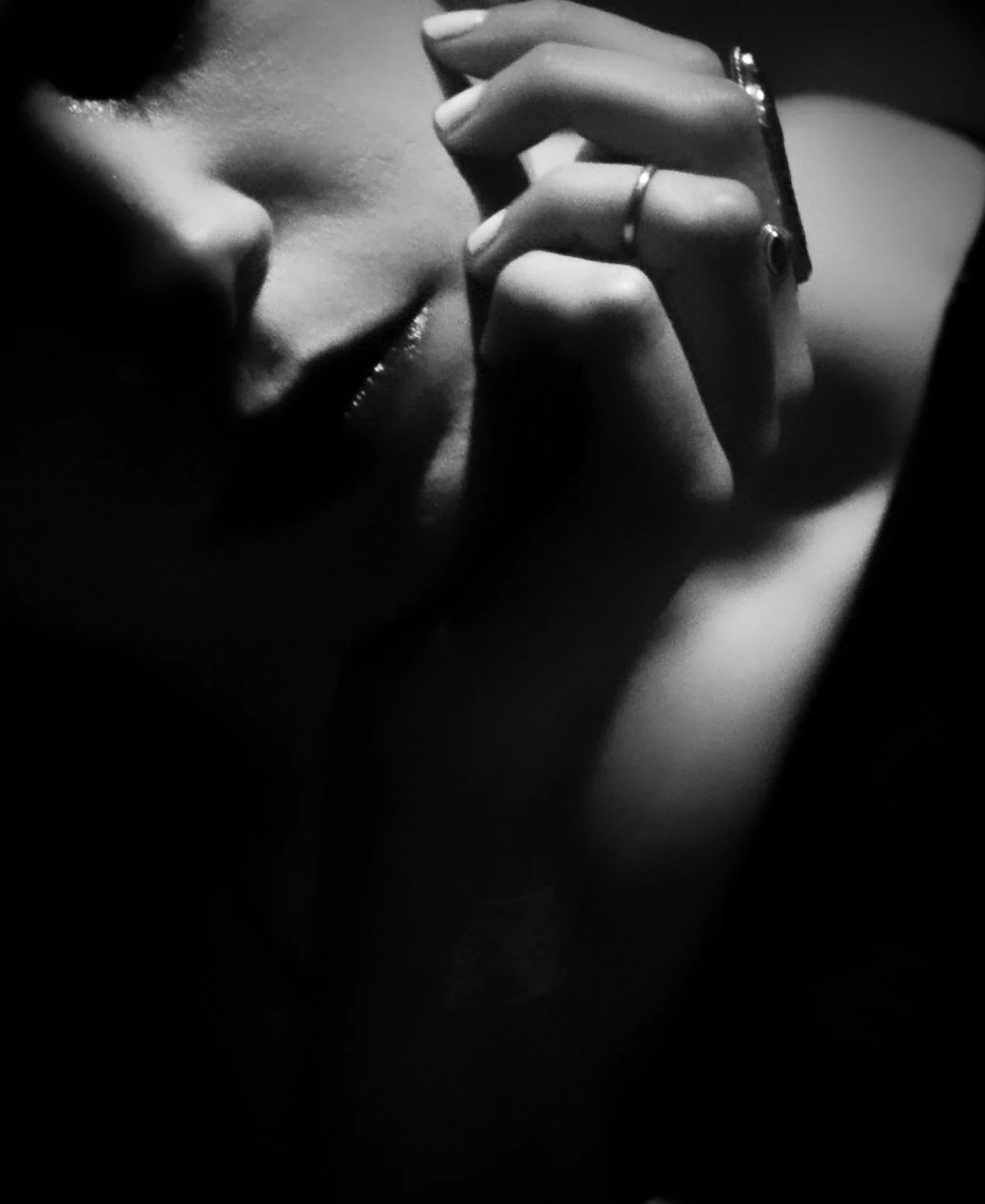 Black and white close-up of a woman with her eyes closed, touching her temple with her fingers, wearing rings on her fingers.