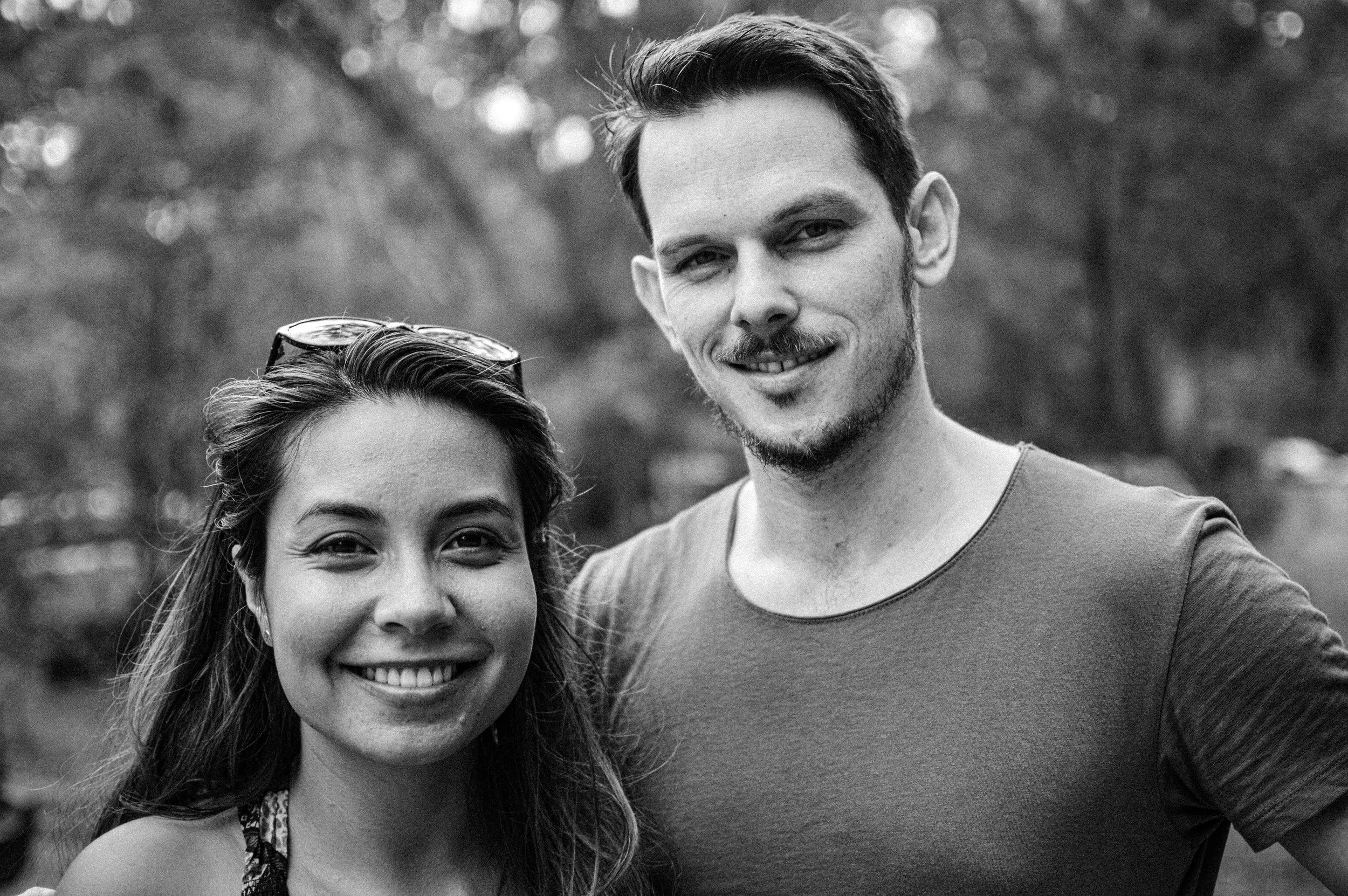 A smiling man and woman outdoors, woman with sunglasses on her head, both facing camera.
