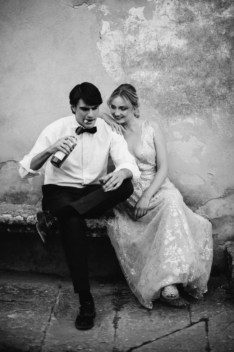 Groom playfully opening a wine bottle with his teeth while the bride laughs, a spontaneous and intimate elopement moment in Tuscany, captured by FunkyBird Weddings Photography.