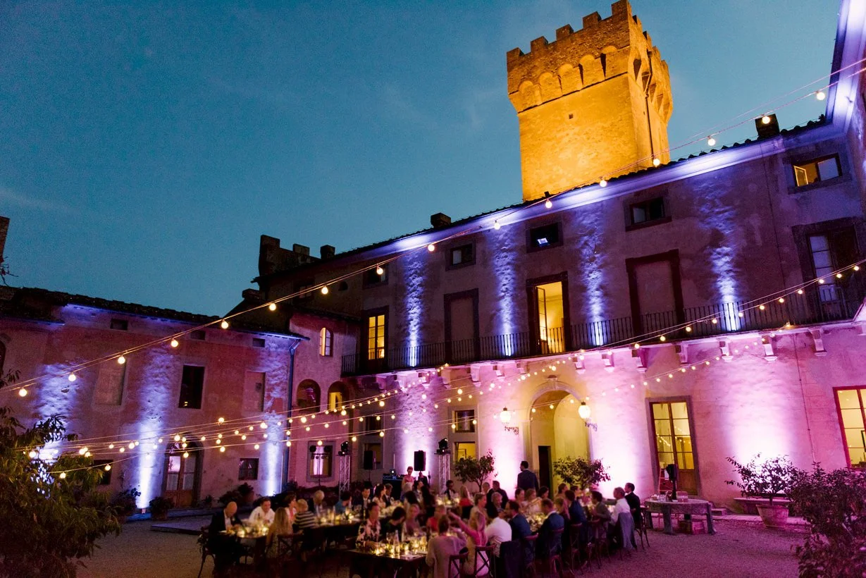 Wedding dinner in a Chianti castle courtyard with round tables and string lights, showing how historic castles create an atmospheric, intimate guest experience during evening celebrations.