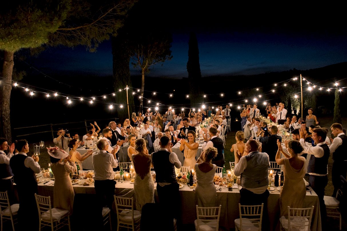 Wedding dinner in Tuscany with guests standing and applauding live musicians, showing coordinated evening flow and reception timing.