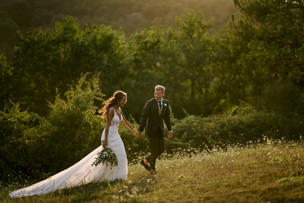 Bride and groom walking through a Tuscan field at sunset during their wedding at Borgo della Meliana, a romantic moment captured by FunkyBird, wedding photographer in Italy.
