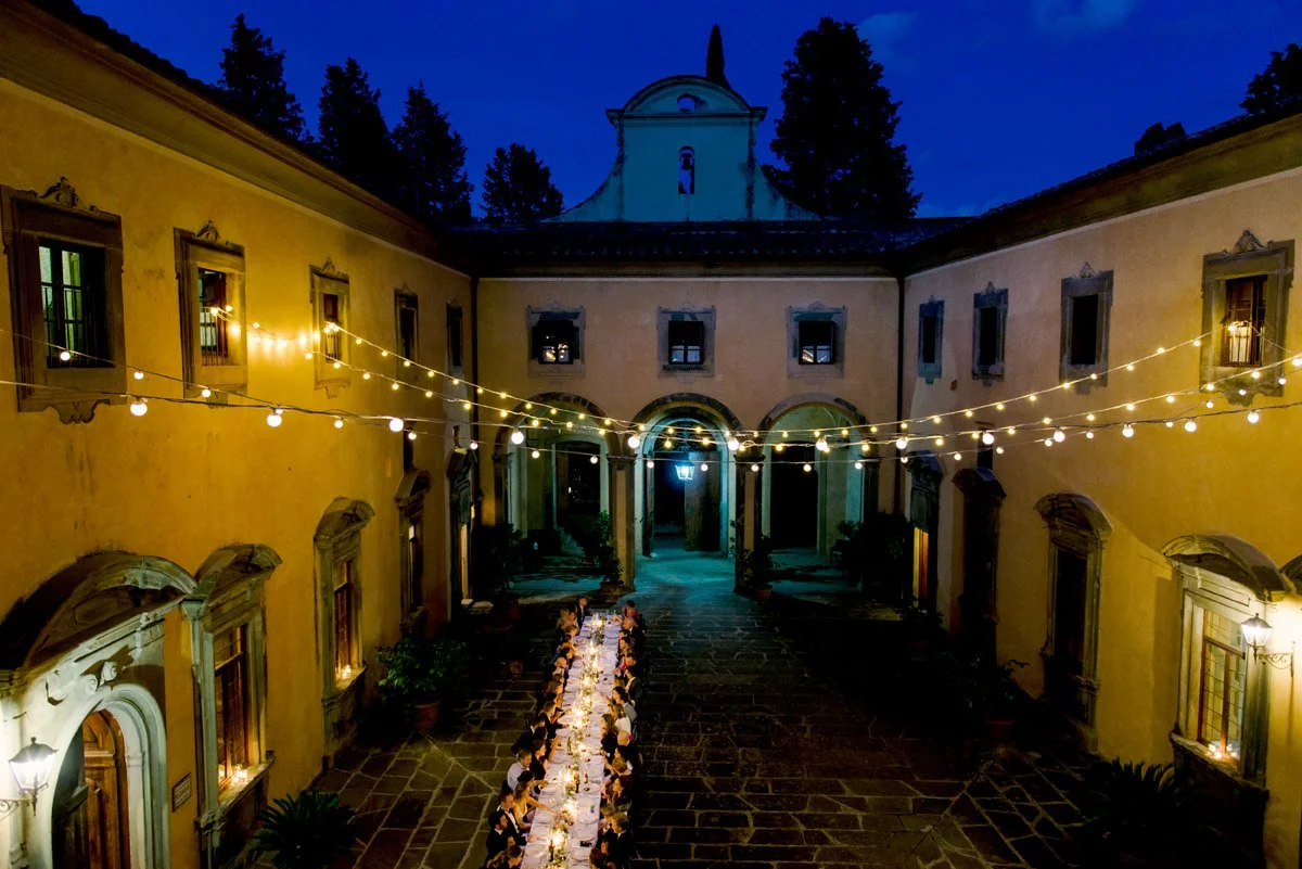 Wedding planner coordinating wedding dinner setup at a Tuscan venue, overseeing table layout, timing, and guest flow before the evening reception begins.
