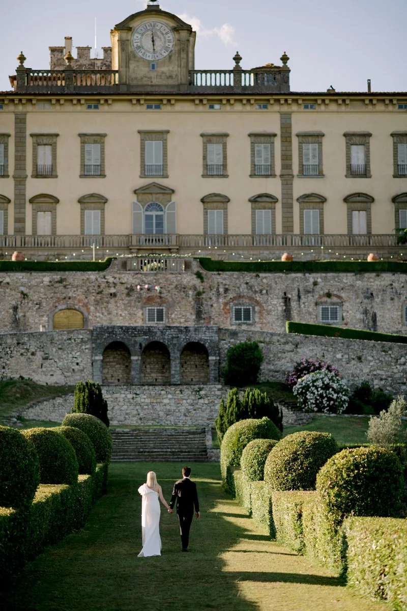 Bride and groom walking together through an Italian garden at Torre a Cona, a romantic and relaxed wedding moment captured by FunkyBird, wedding photographer in Tuscany.