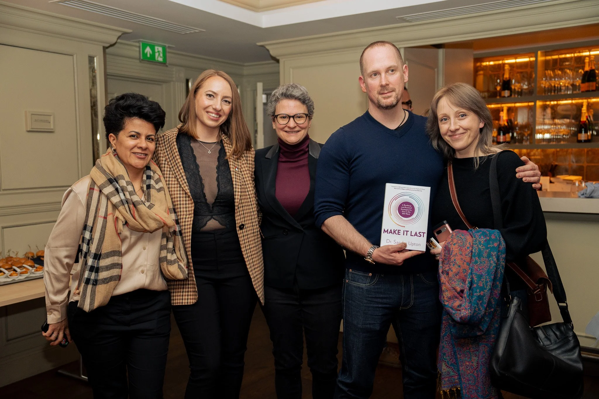Group of five people smiling at an event, with one person holding a book titled 'Make It Last' by Dr. Sally Upton.