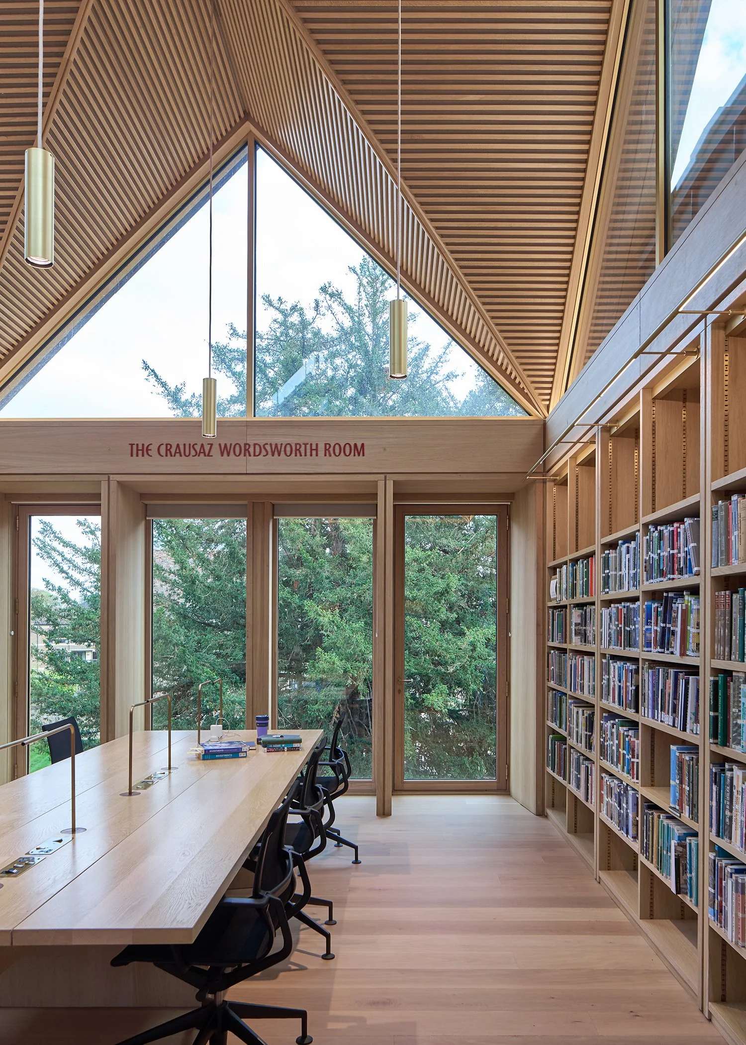 Modern library room with large windows, wooden ceiling, bookshelves, and a long table with chairs, labeled 'The Crausaz Wordsworth Room.'