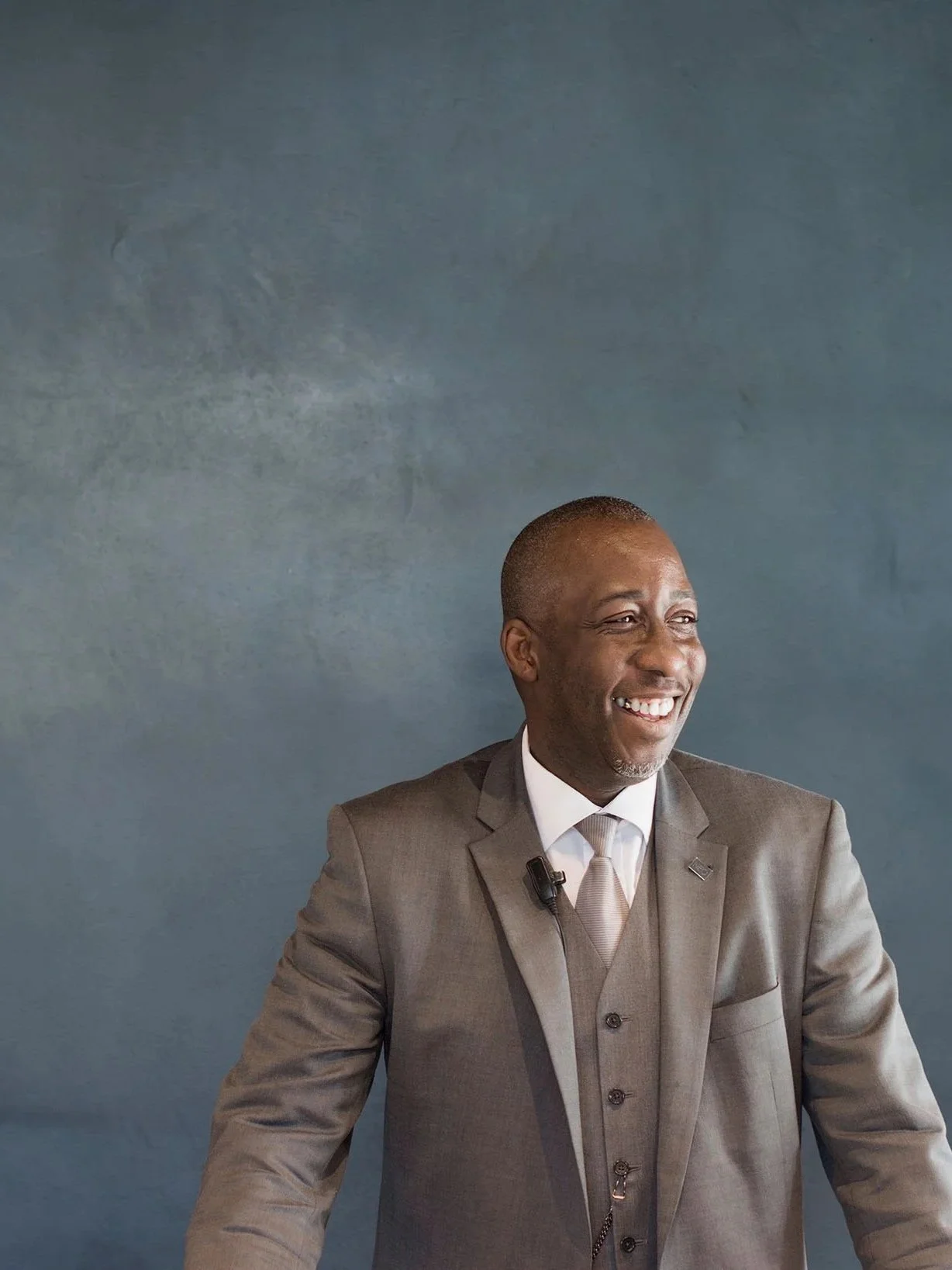 Smiling man in a suit standing against a gray background.