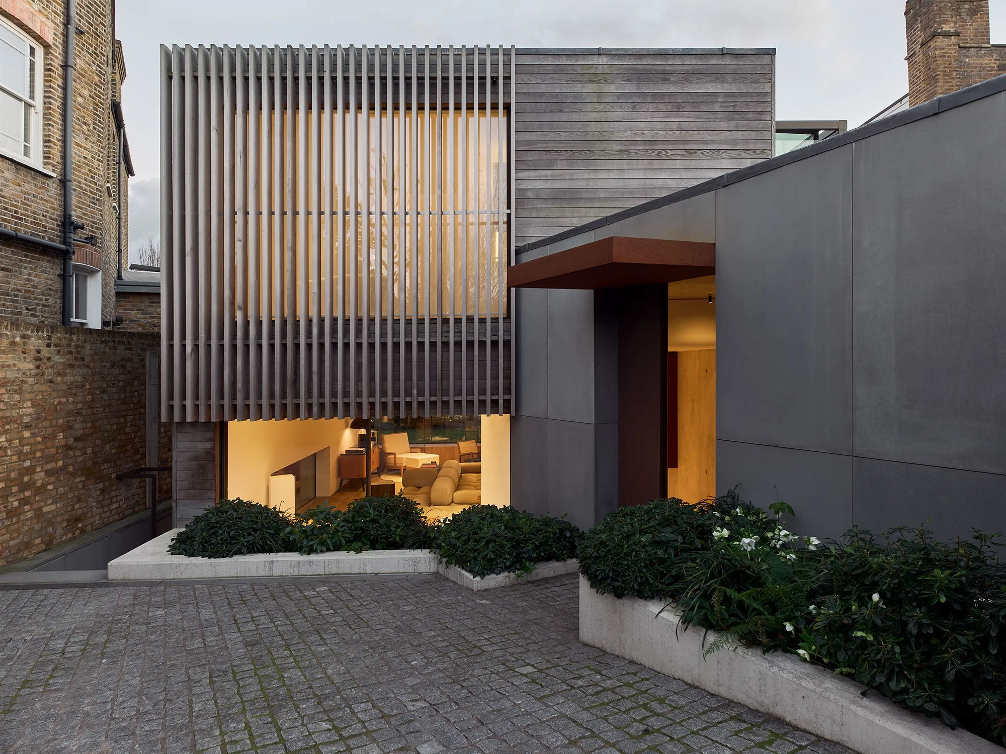 Modern house exterior with vertical wooden slats, large windows, concrete facade, and landscaped plants.
