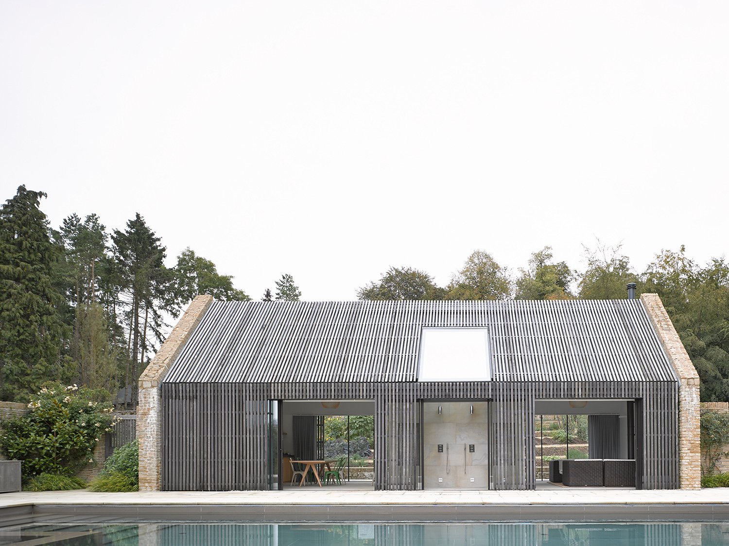 Modern pool house with slatted wooden exterior, glass doors, and surrounded by trees.