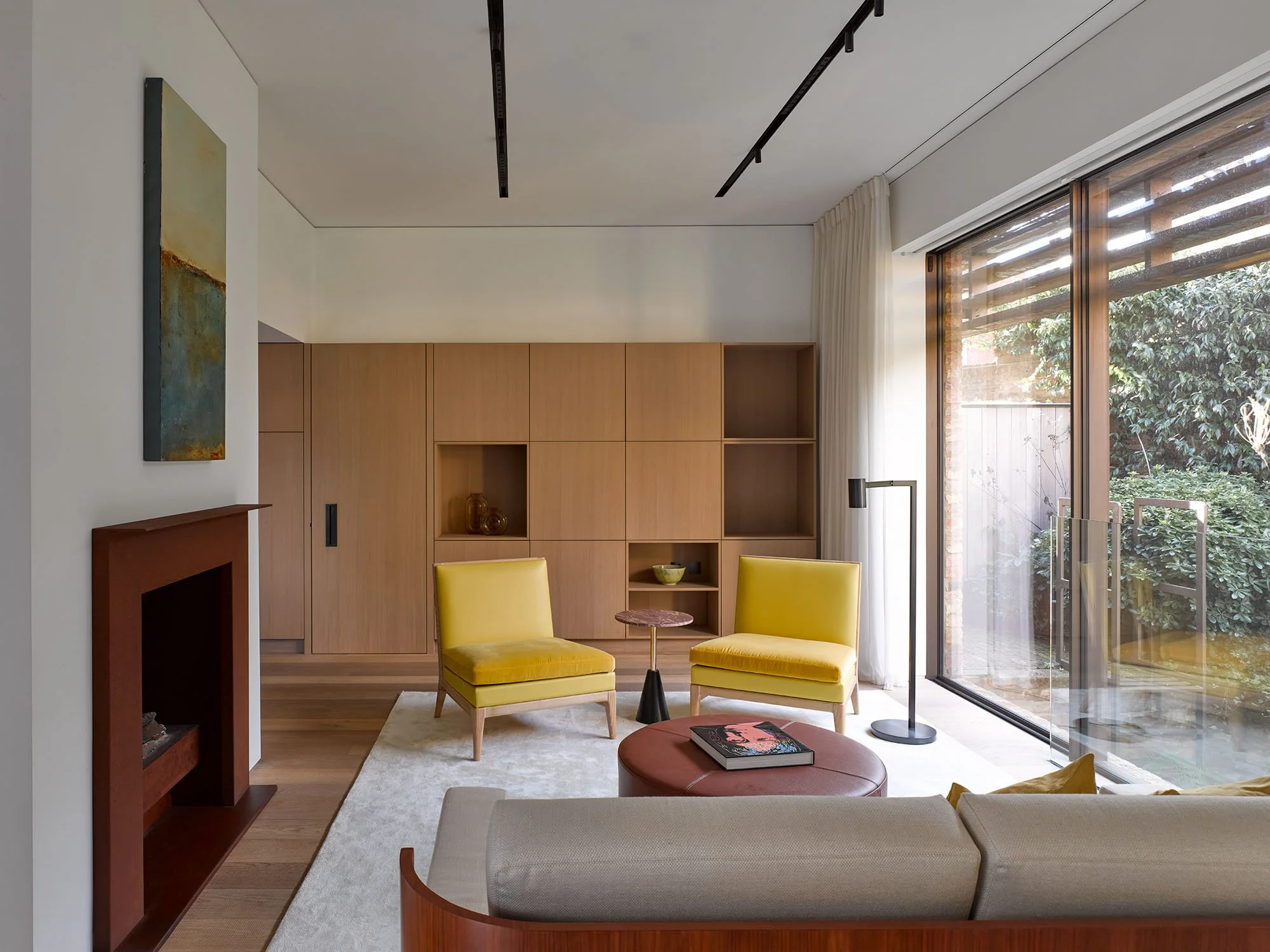 Modern living room with a minimalist design, featuring a fireplace, wooden cabinets, yellow chairs, glass sliding door, and contemporary artwork.