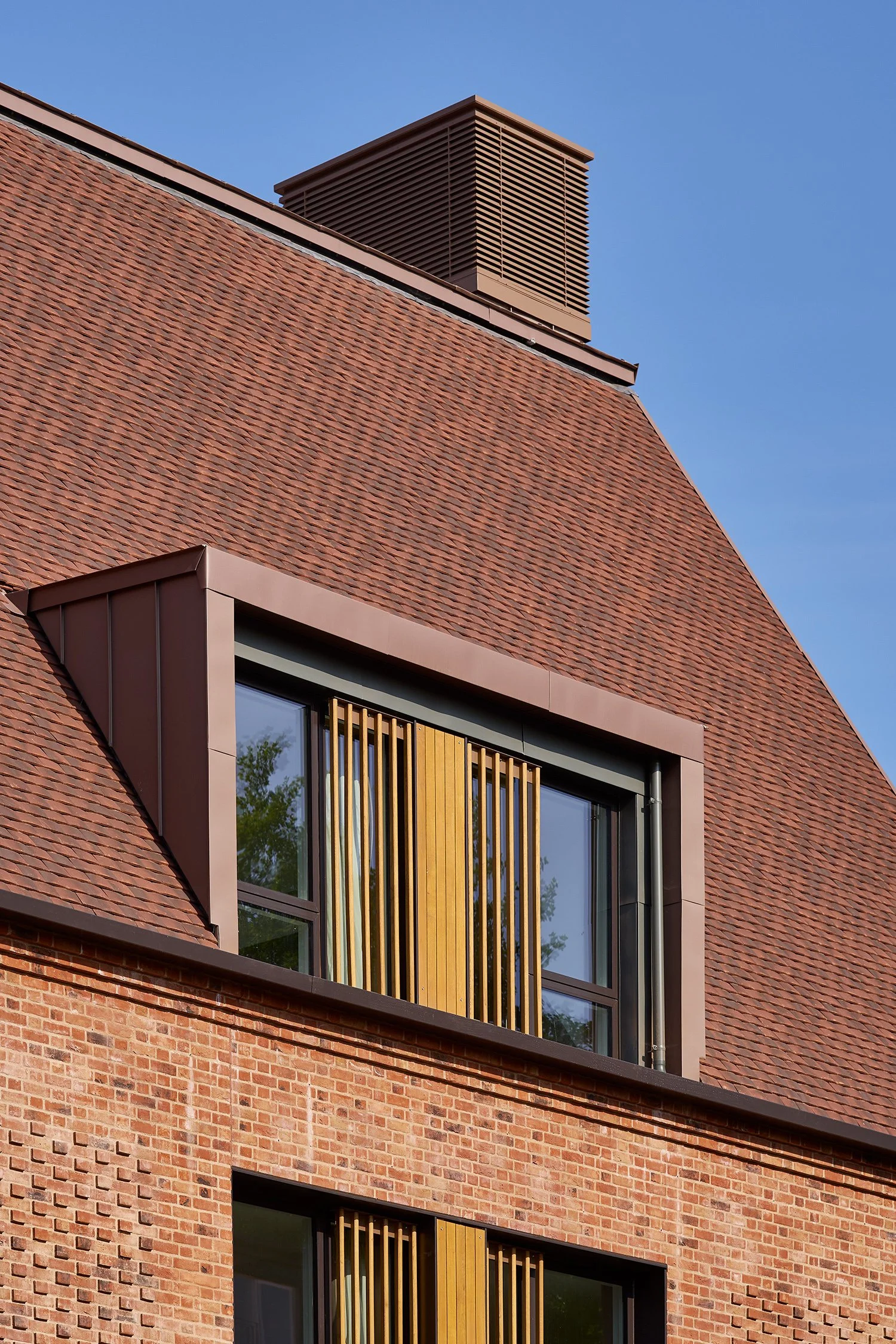 Close-up of a modern brick building with wooden window coverings and a metal roof, under a clear blue sky.