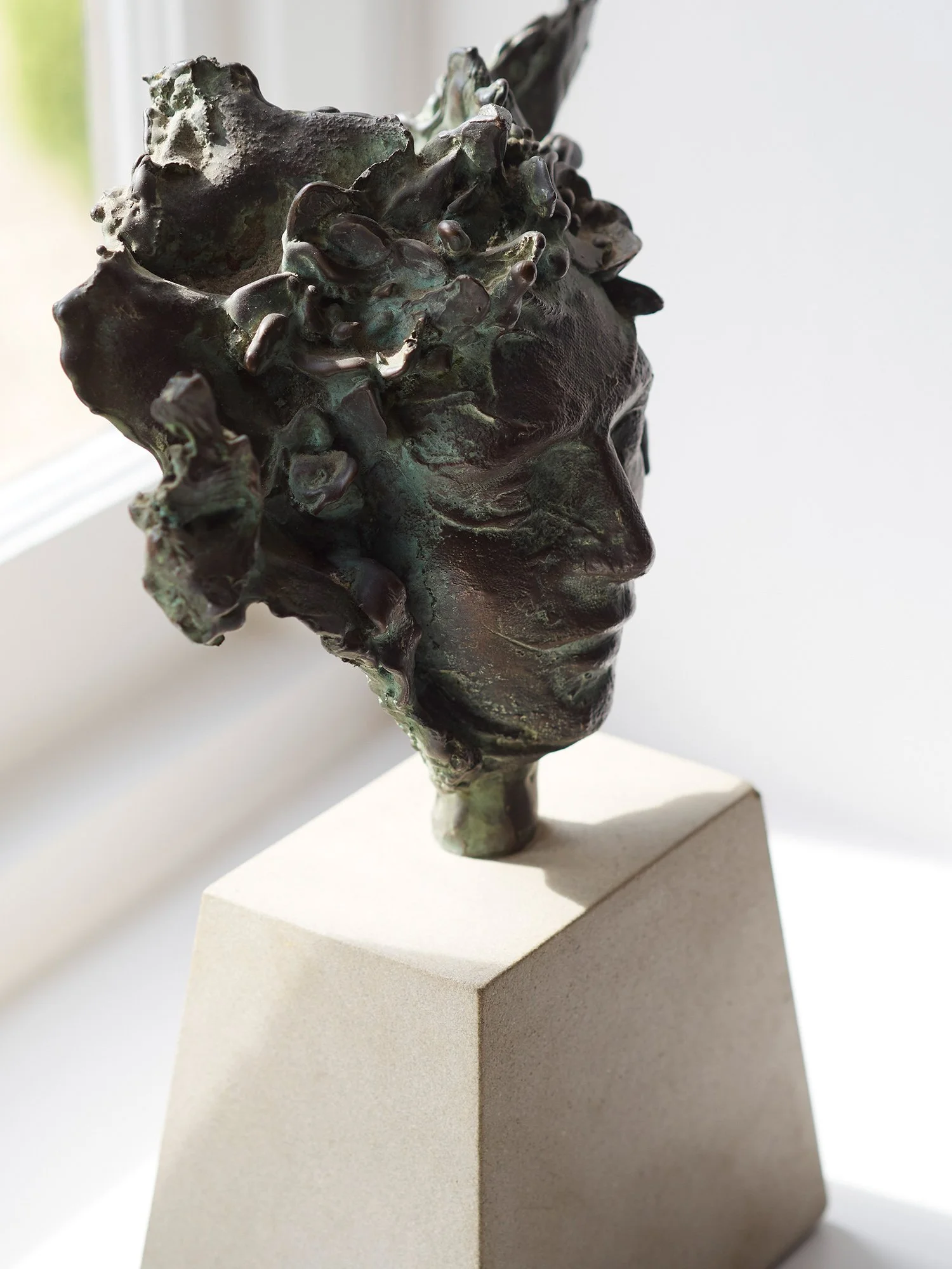 Bronze sculpture of a human head with curly hair, mounted on a beige pedestal.