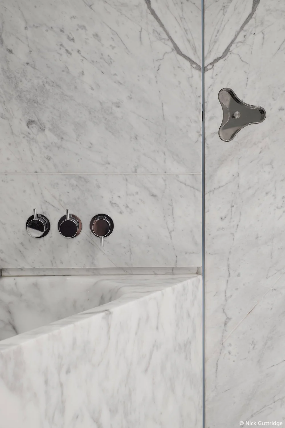 Marble bathroom wall with modern metal faucet handles and exposed tub edge.