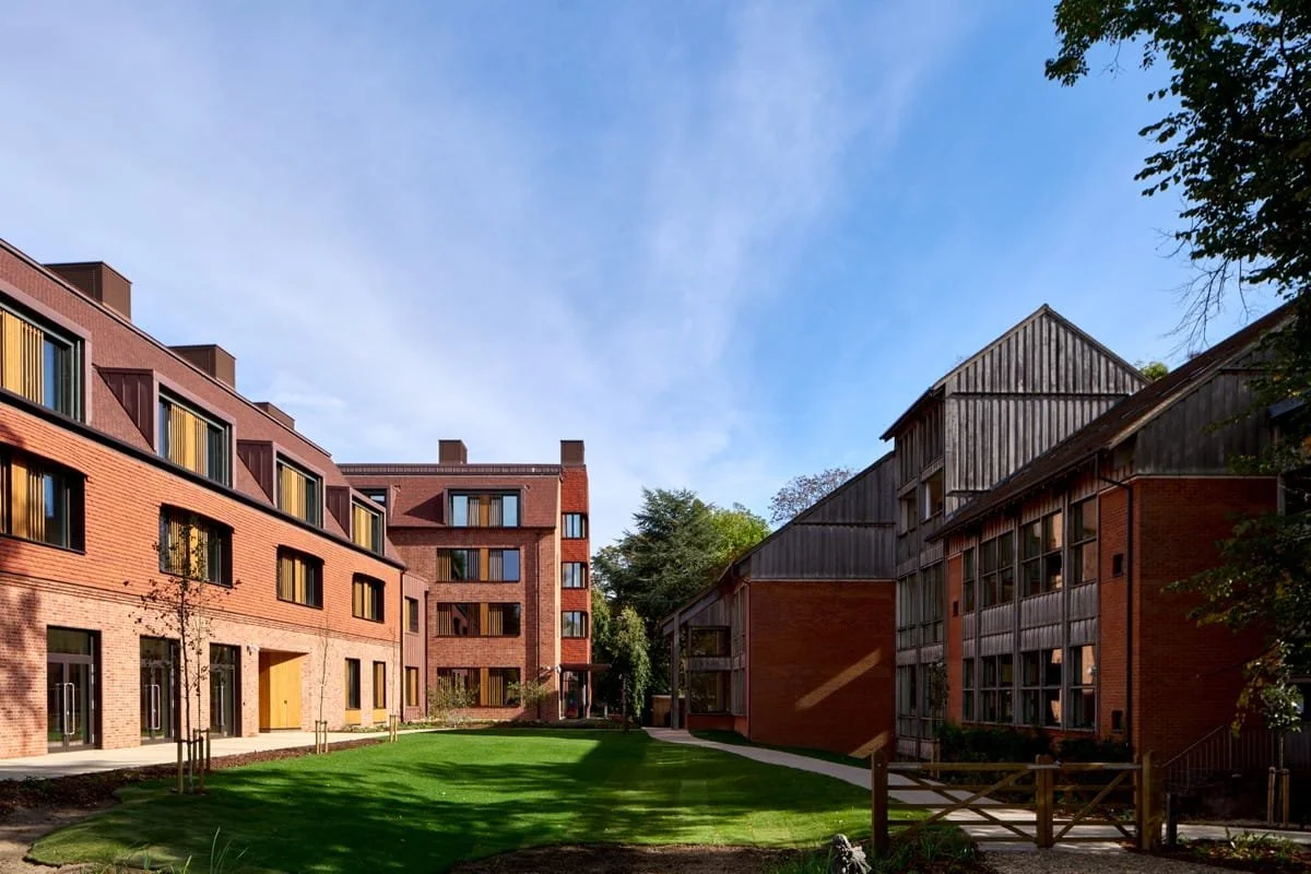 A residential courtyard with green grass, surrounded by brick and wooden apartment buildings, under a blue sky.