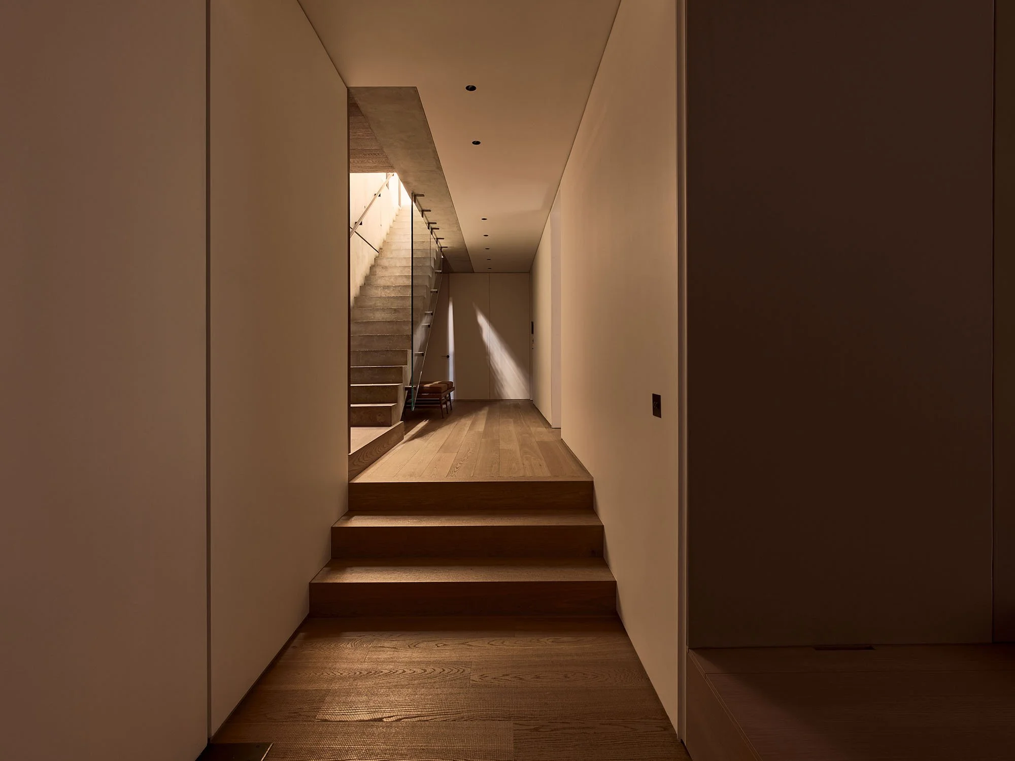 Minimalist hallway with staircase and wooden floor, softly lit by natural light.