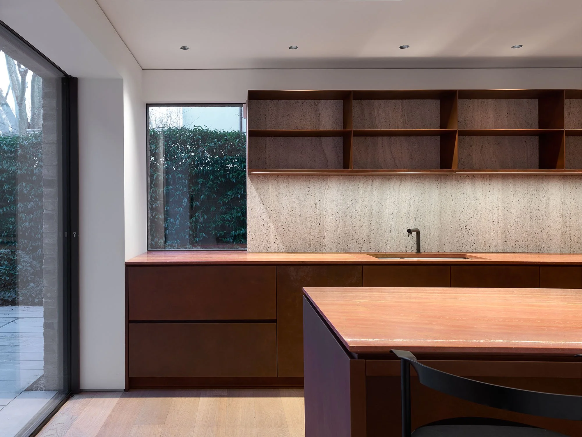 Modern kitchen interior with wooden countertops, open shelves, and a minimalist design. Large window provides natural light, with a view of greenery outside. Neutral color palette.