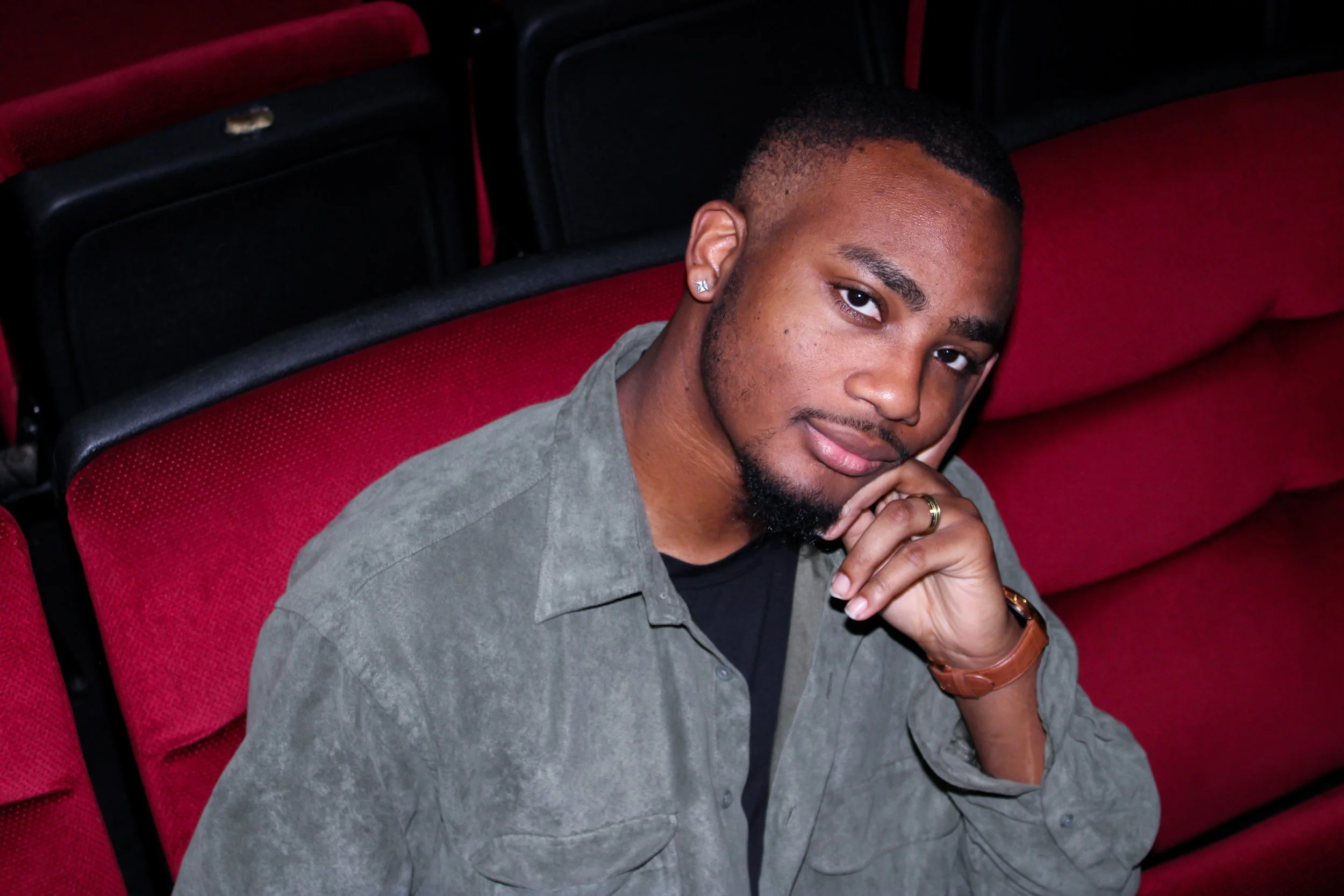Close-up of a woman with curly hair and light brown eyes, smiling and wearing a green top.