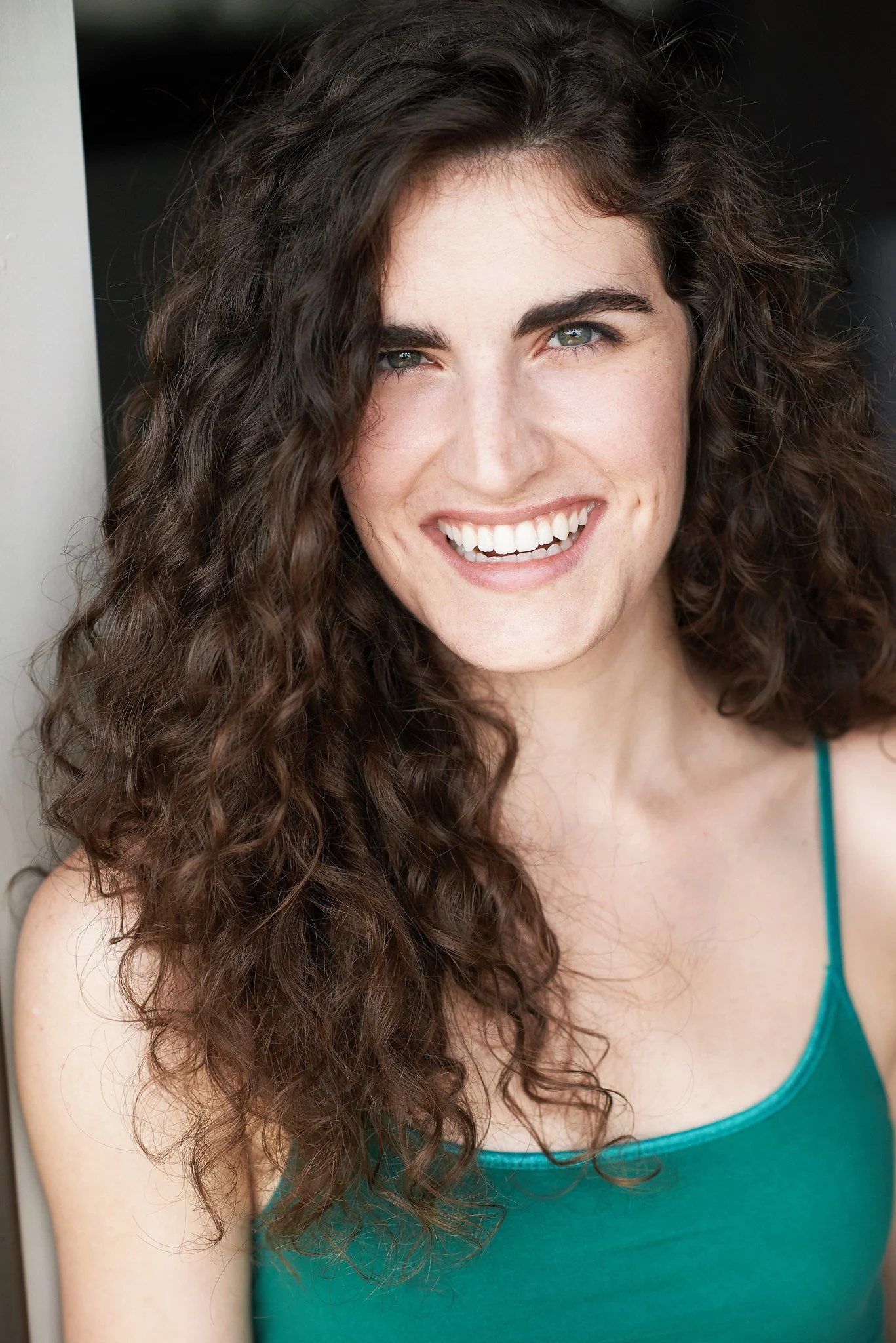 A woman with long, curly brown hair and blue eyes smiling.