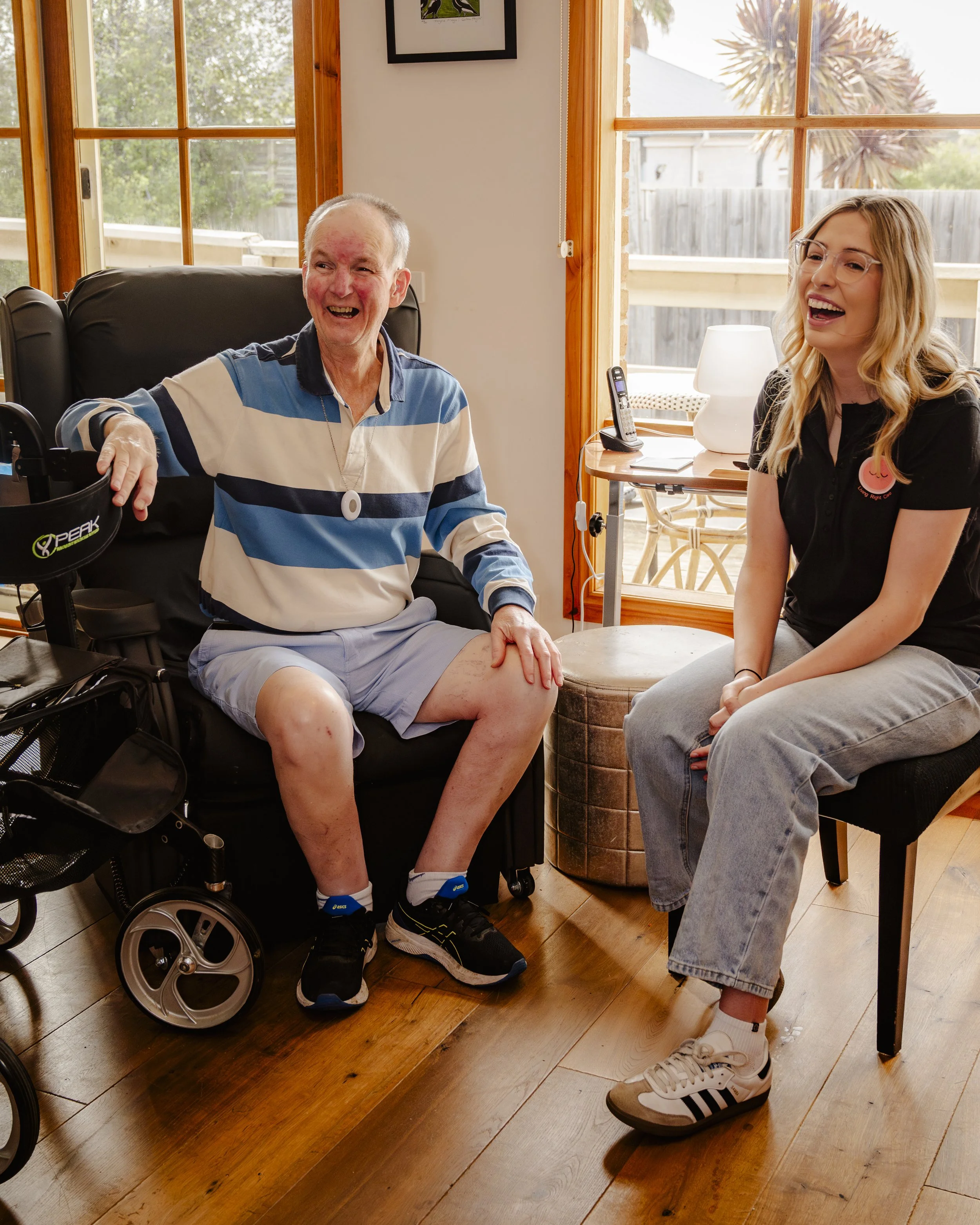 A senior man with a wheelchair engaging in a conversation with a young woman in a living room.