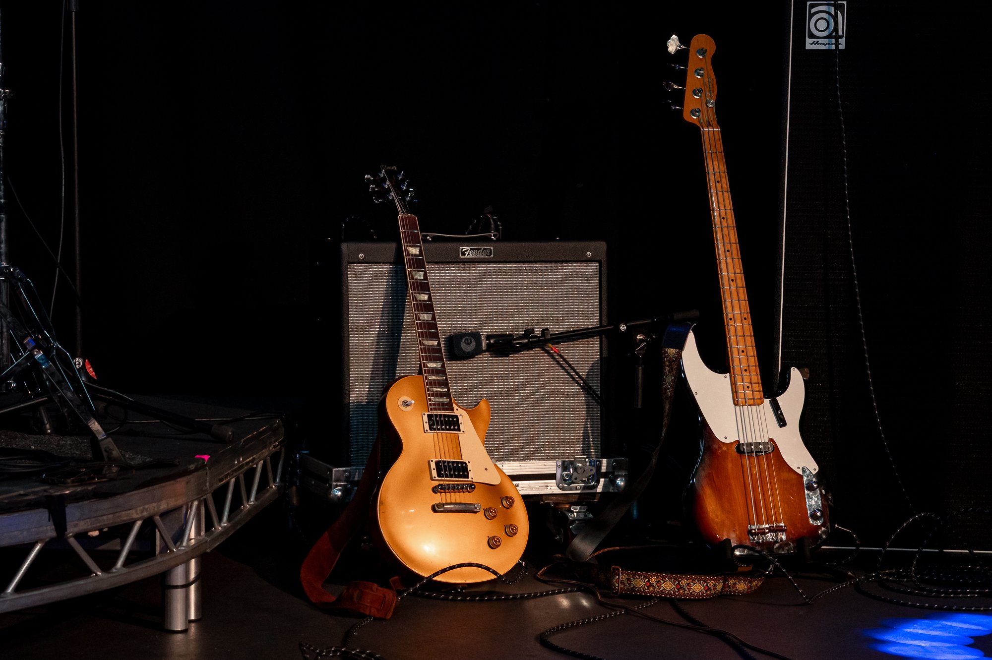 Electric guitar, bass guitar, and amplifier on stage with dark background and cables on floor.
