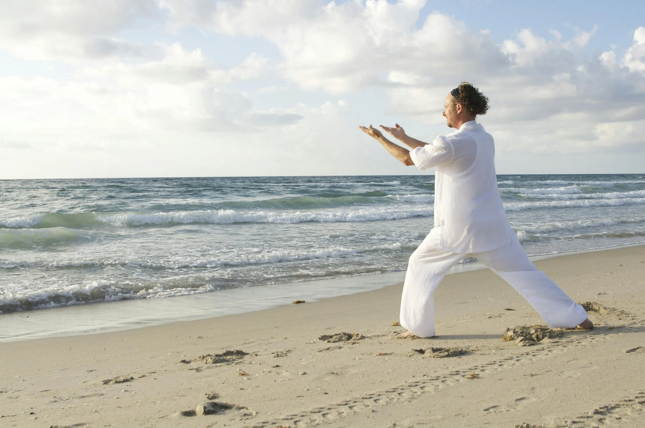 Person wearing all white doing tai chi on a beach