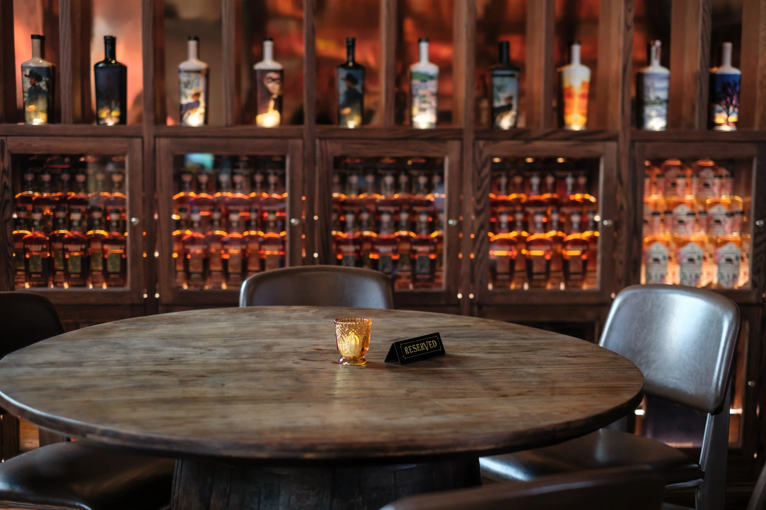 A reserved table at The Last Refuge surrounded by illuminated bourbon displays, reflecting an upscale dining and cocktail experience in Louisville’s premier whiskey bar.