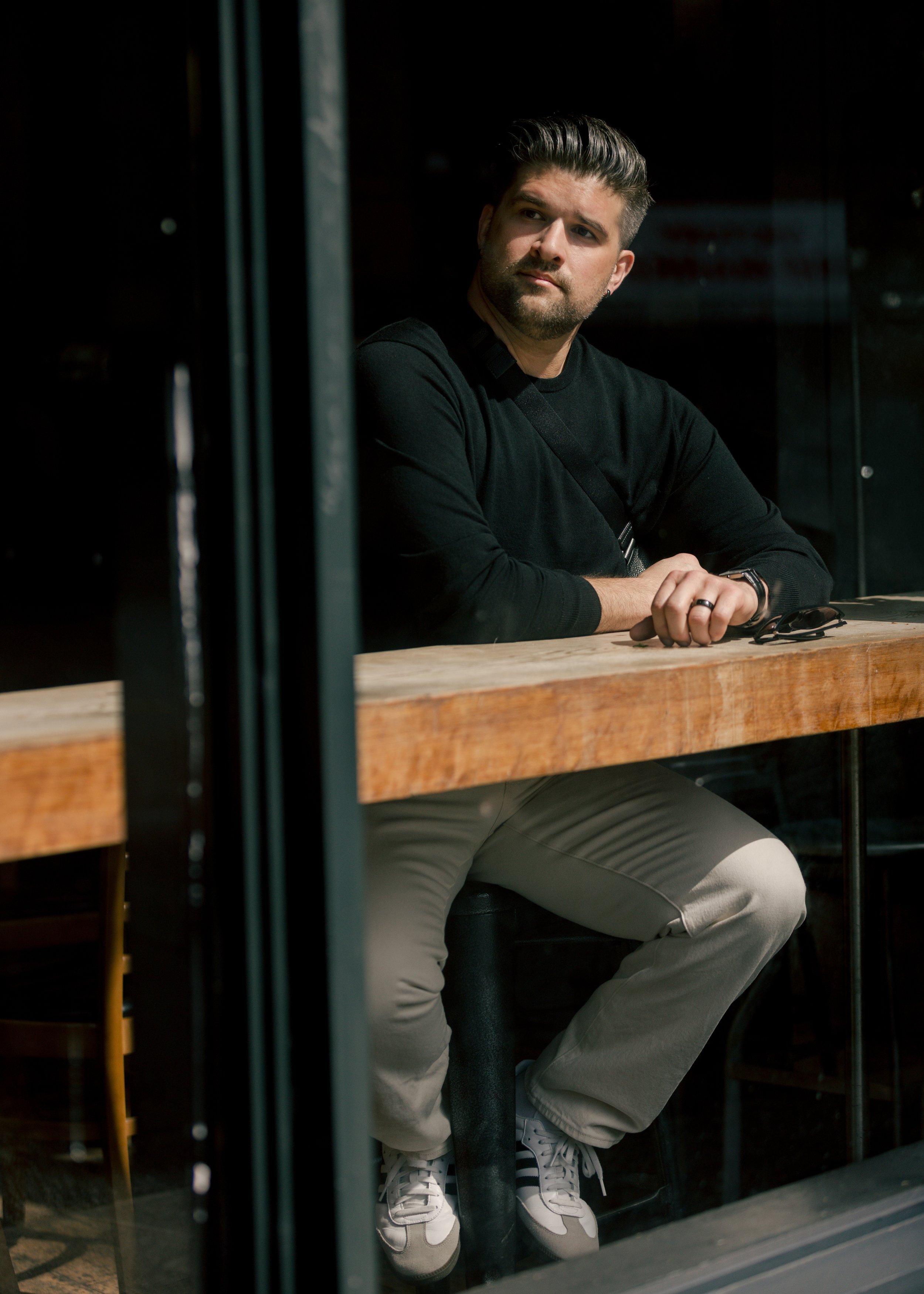 Person seated at a wooden table looking out a window in a cafe environment.