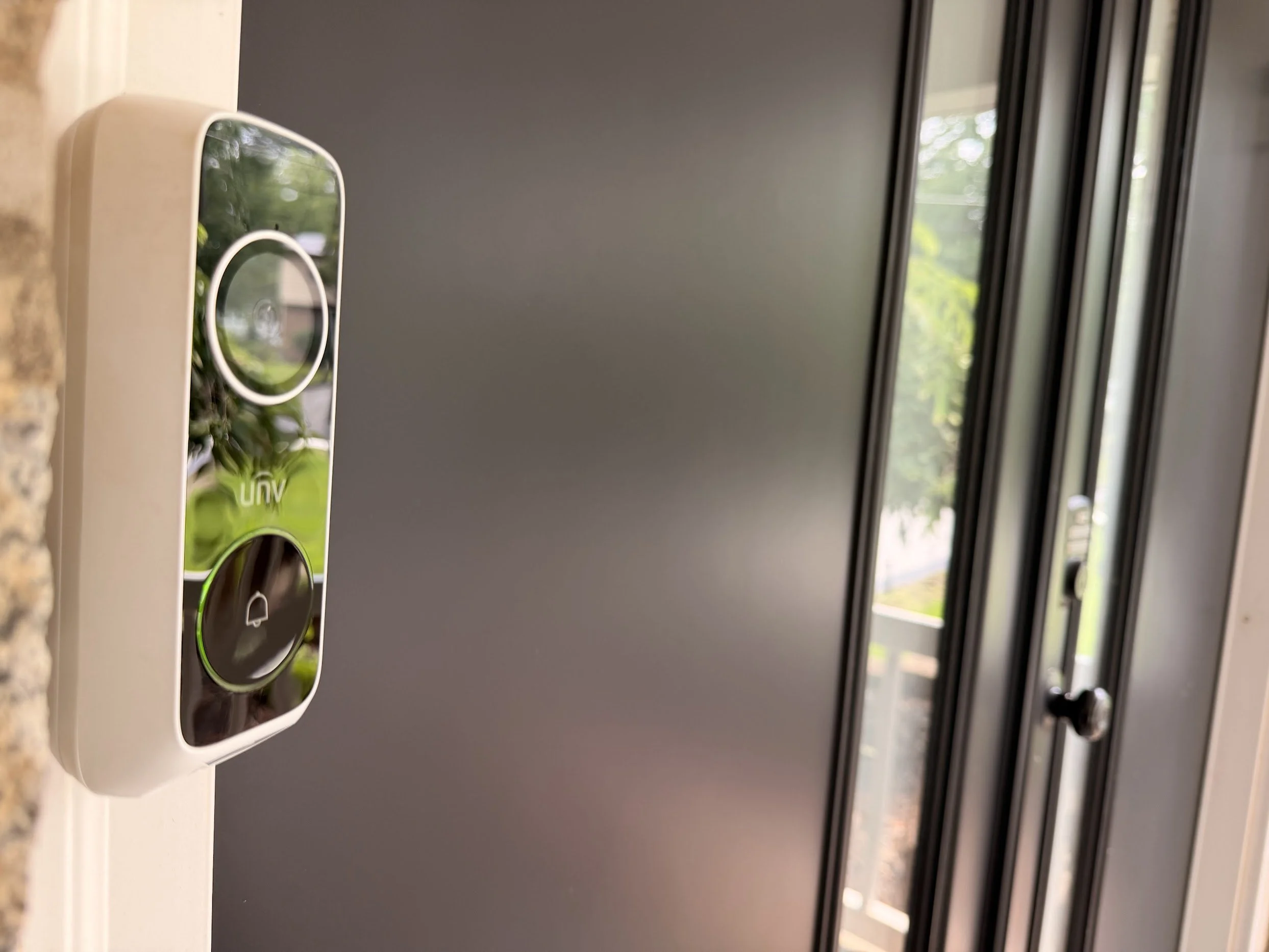 Electronic door lock with green illuminated handle and camera on beige wall, blurred background of hallway.