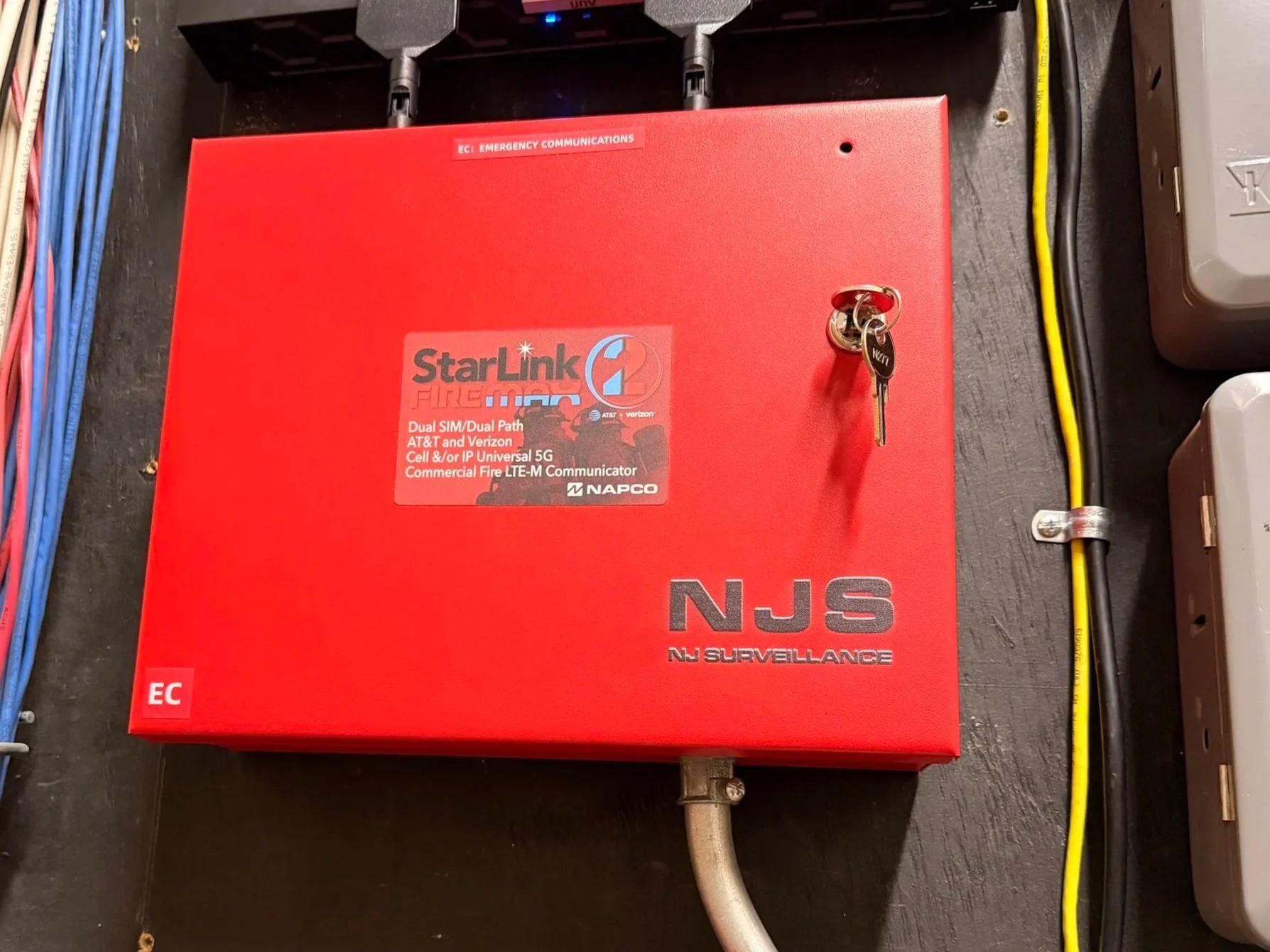 Red StarLink device mounted on a wall, labeled 'NJS' for New Jersey Surveillance, with antennas on top, used for emergency alert communication.