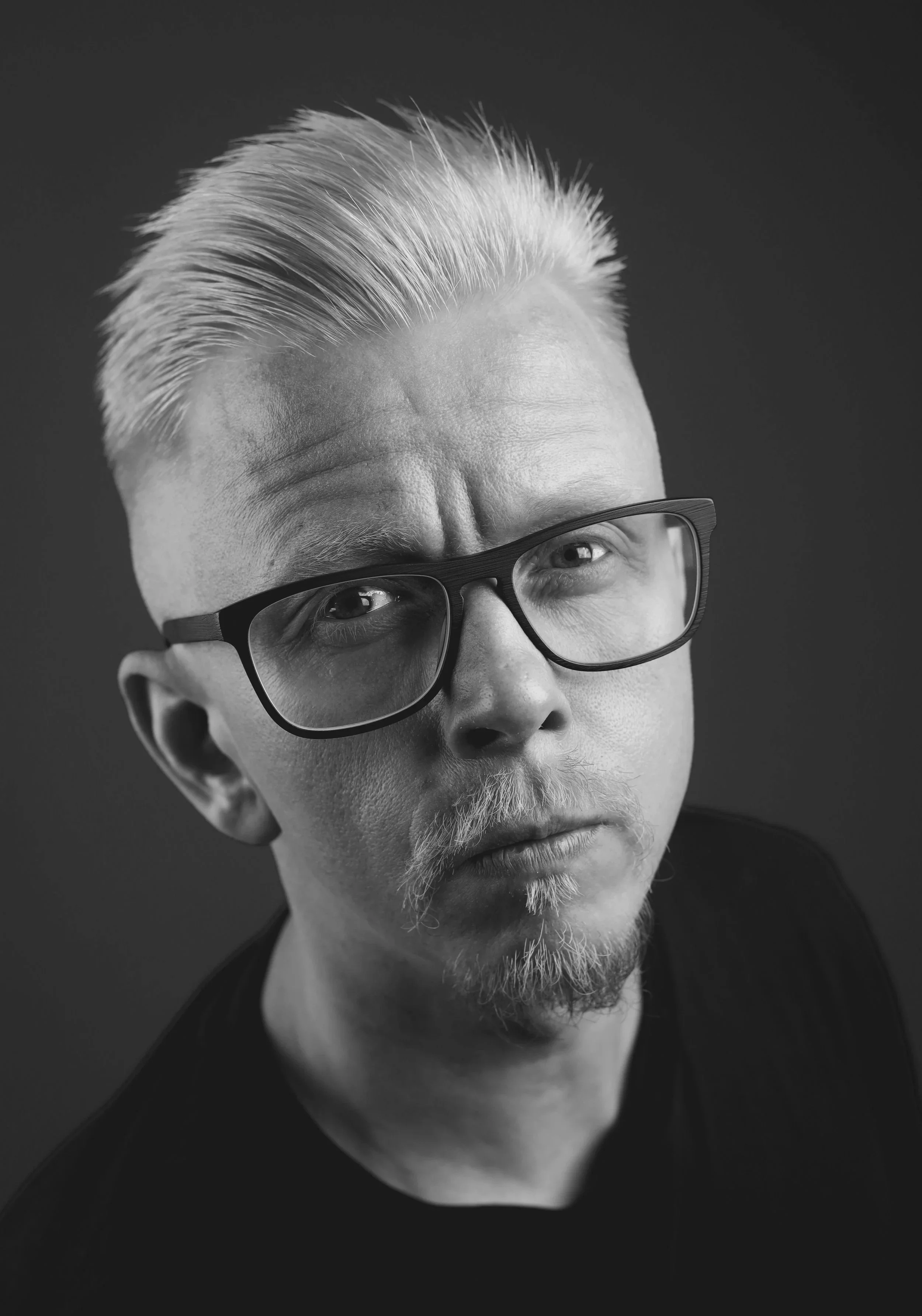 Mustavalkoinen muotokuva silmälasipäisestä miehestä studiossa