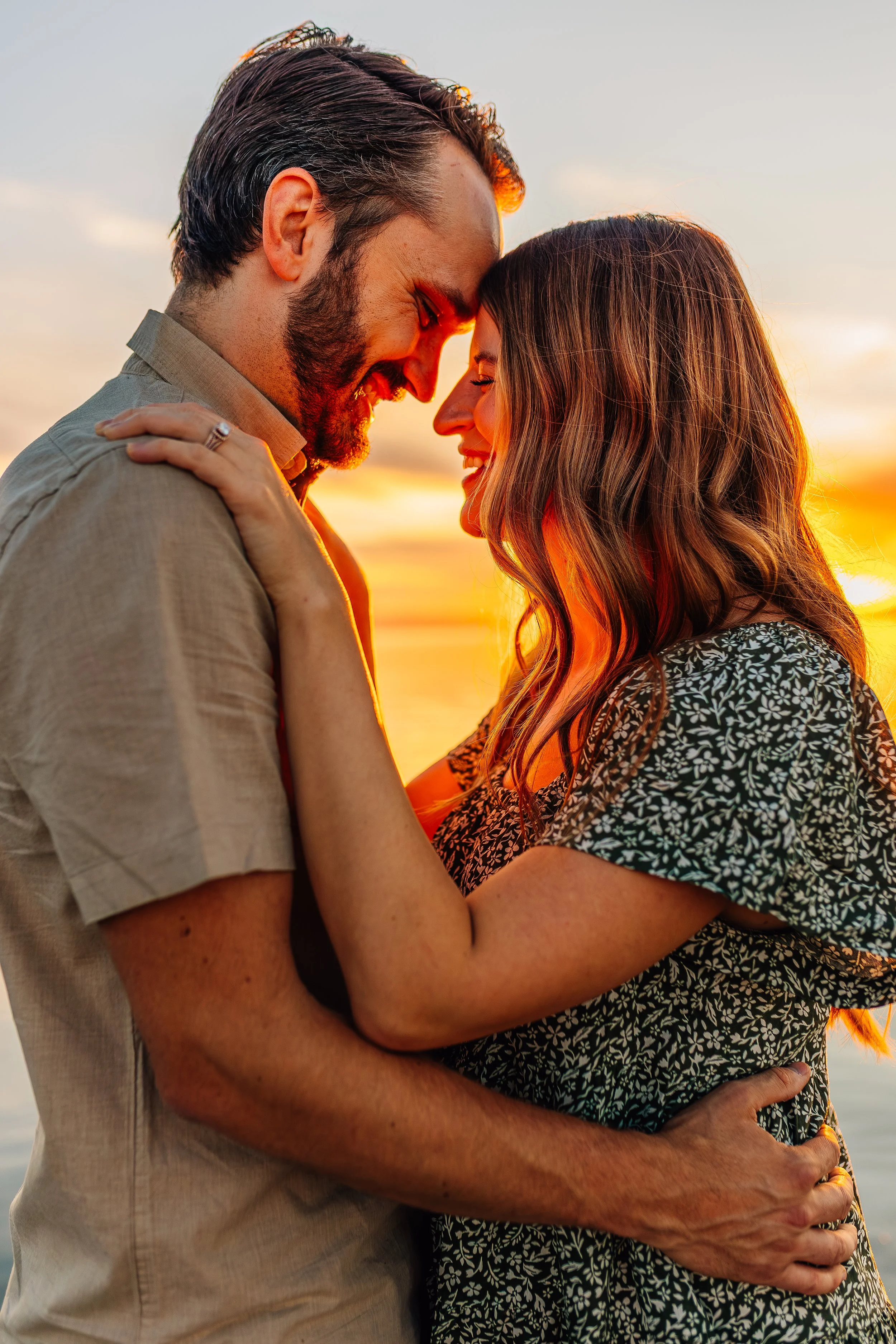 A couple embracing with their foreheads touching at sunset, smiling at each other.