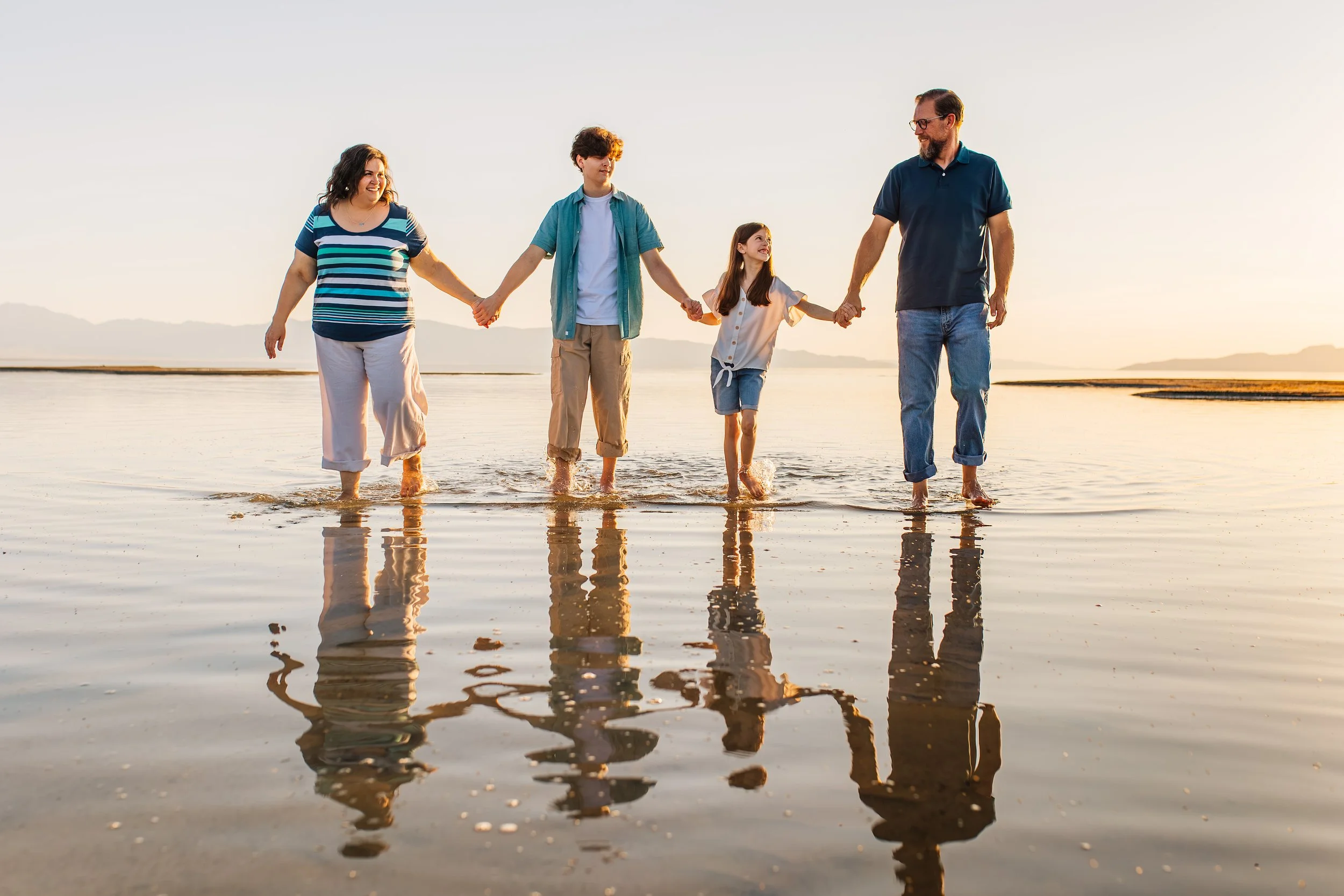 A family of five holding hands and walking on a beach at sunset.