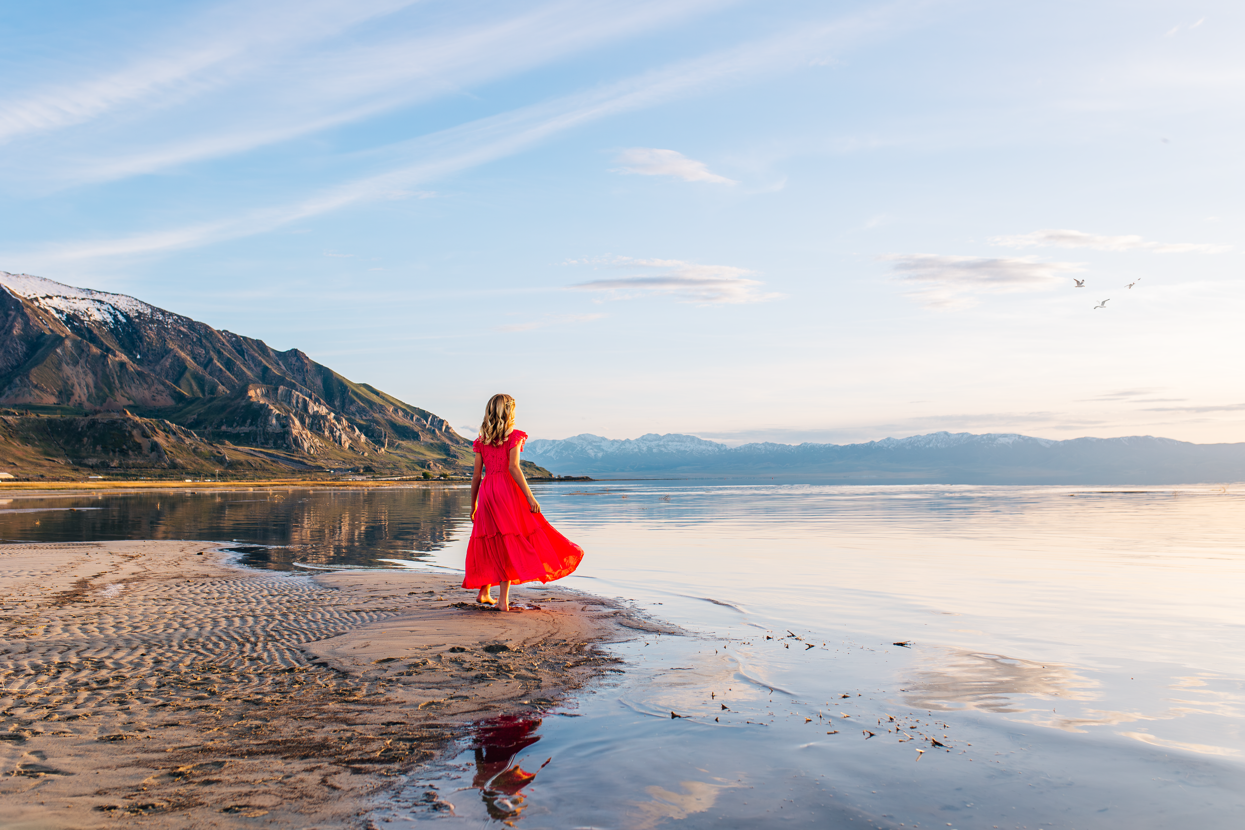 Documentary-style family photography at the Great Salt Lake in Salt Lake County featuring a woman in a red dress walking along the shoreline at sunset, capturing connection and privacy-focused storytelling.