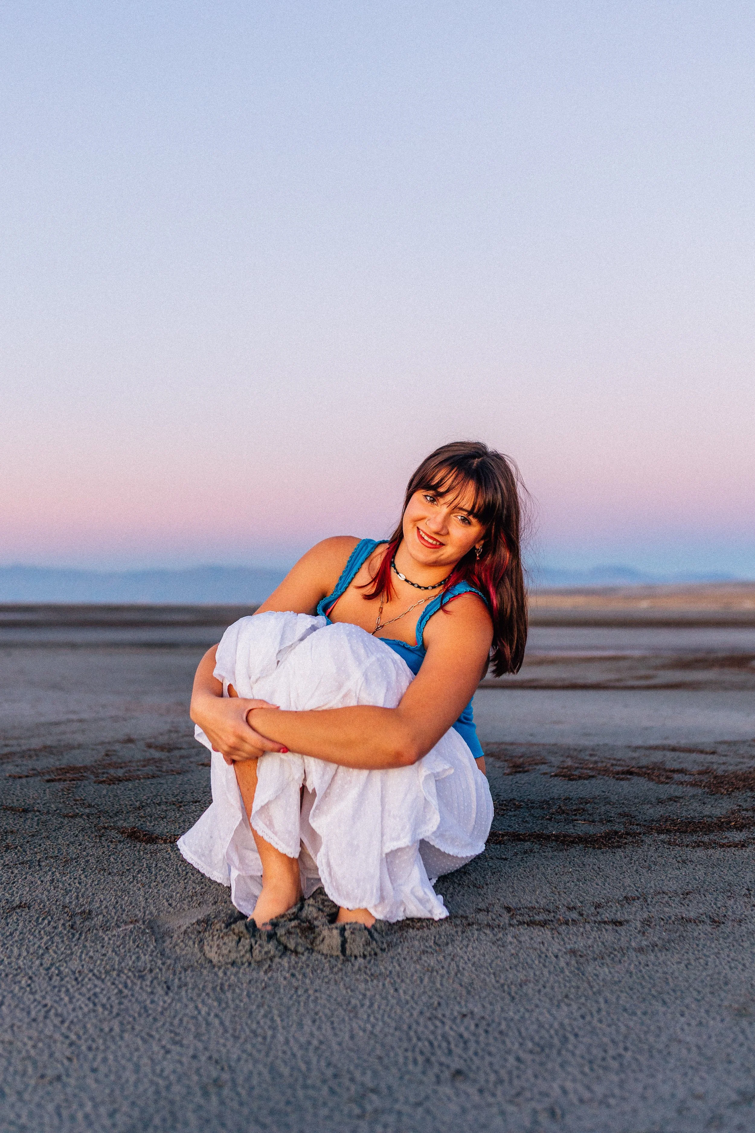 A young boy with dark hair smiling on a sandy beach during sunset.